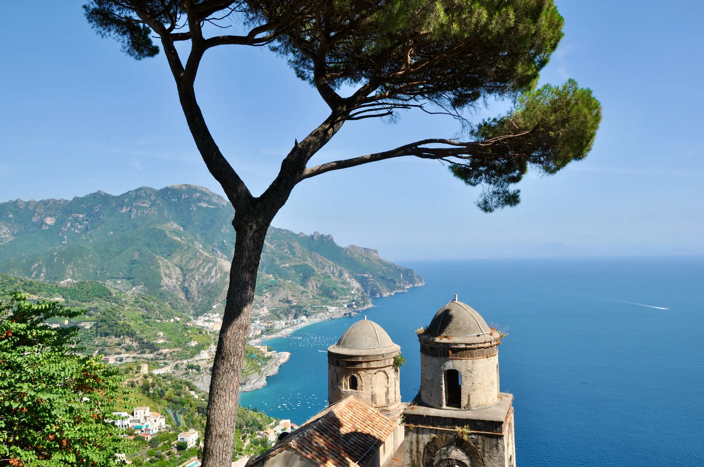 View of Amalfi Coast, Italy, from Ravello with iconic tree, historic buildings, and turquoise sea on a clear day.
