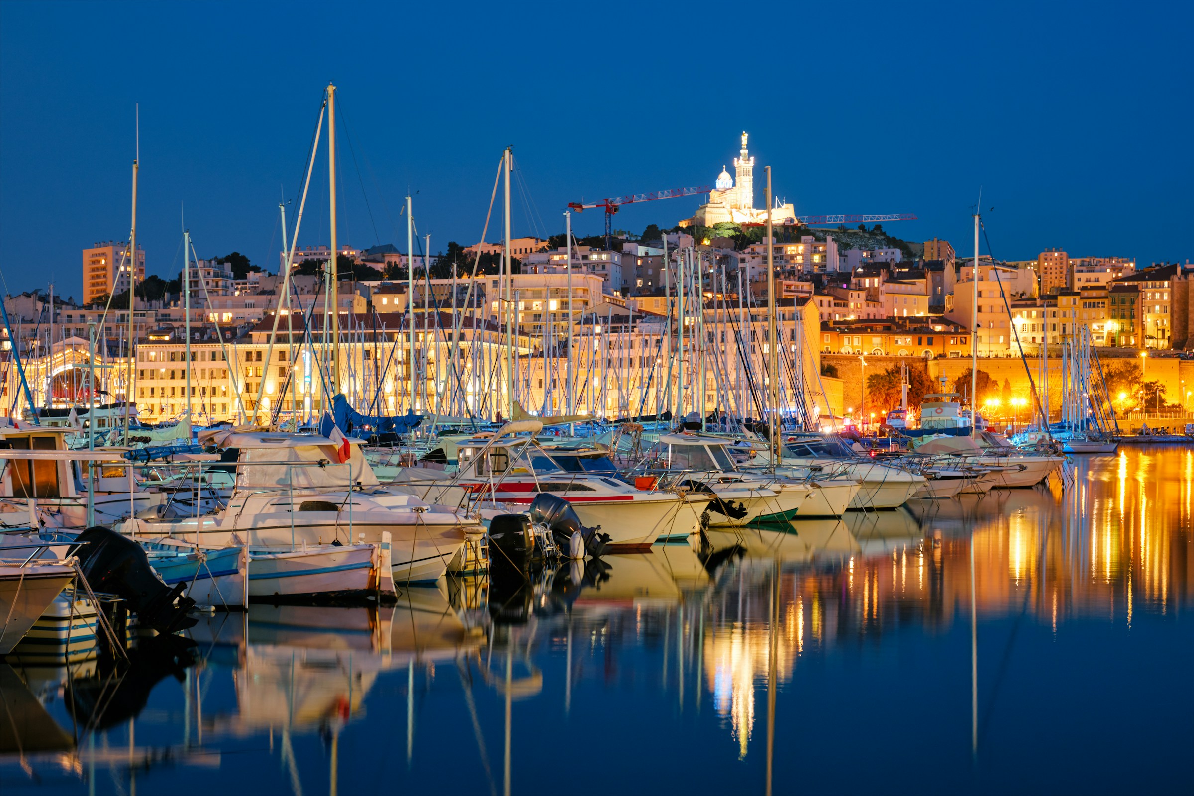 Boats in the french riviera harbor during the evening with an illuminated city in the background