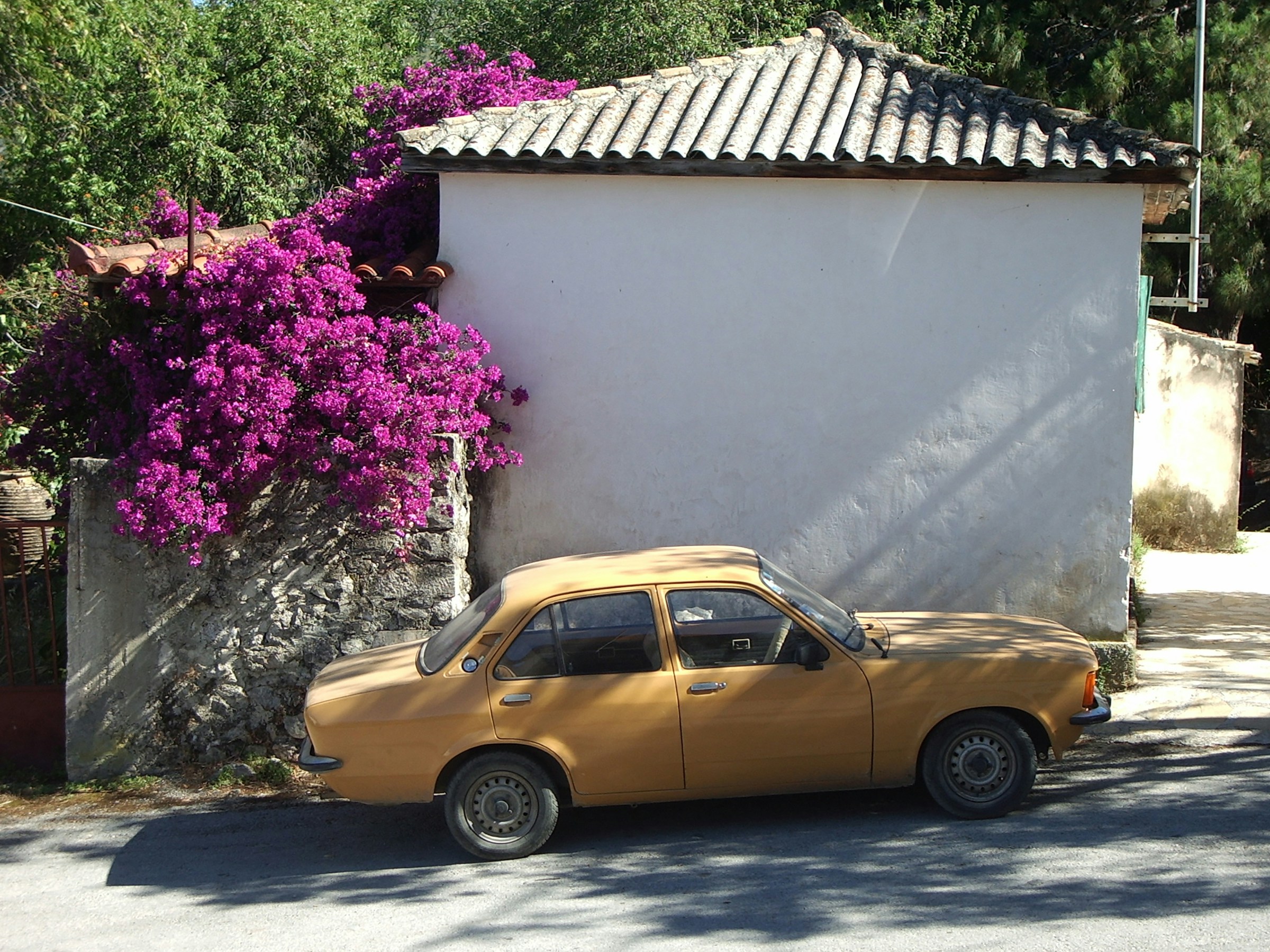 Vintage yellow car parked beside a white building with vibrant purple bougainvillea in Zakynthos.