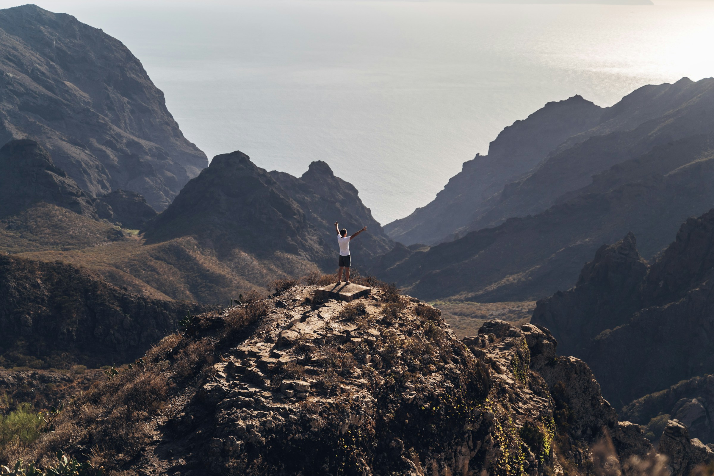 mand stående på en klippe og kigger på naturen og bjergene ved solnedgang på Tenerife