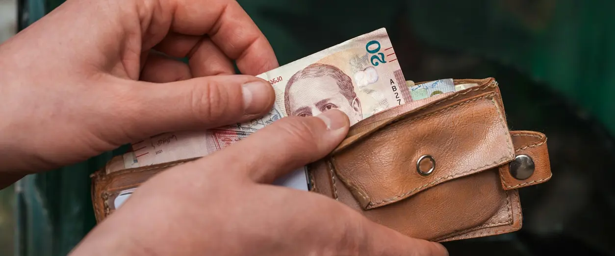 Person tar upp en sedel ur en brun plånbok för att betala med kontanter.