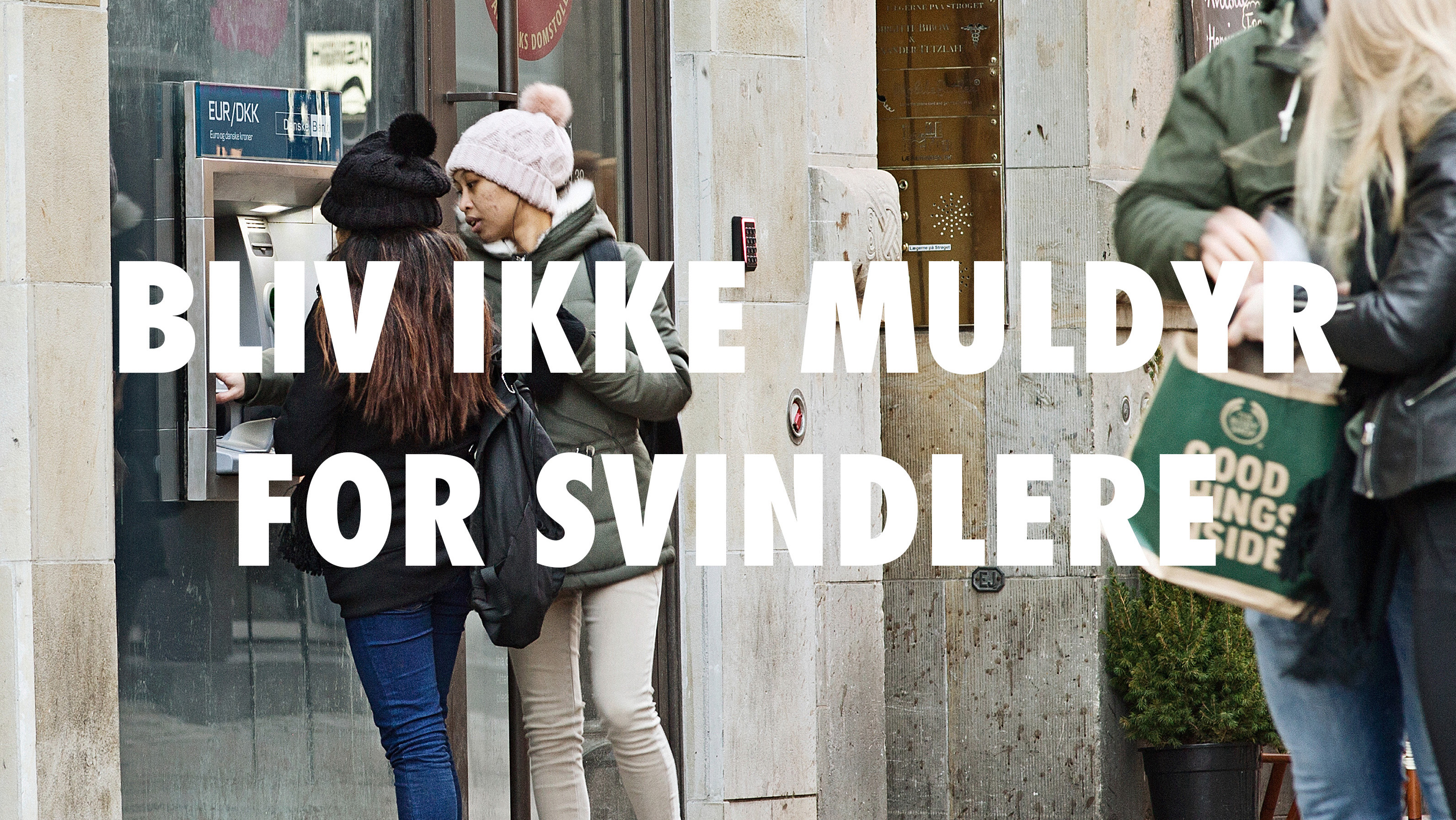 To kvinder hæver penge ved en hæveautomat med teksten "Bliv ikke muldyr for svindlere" over motivet, advarsel mod økonomisk svindel i Danmark