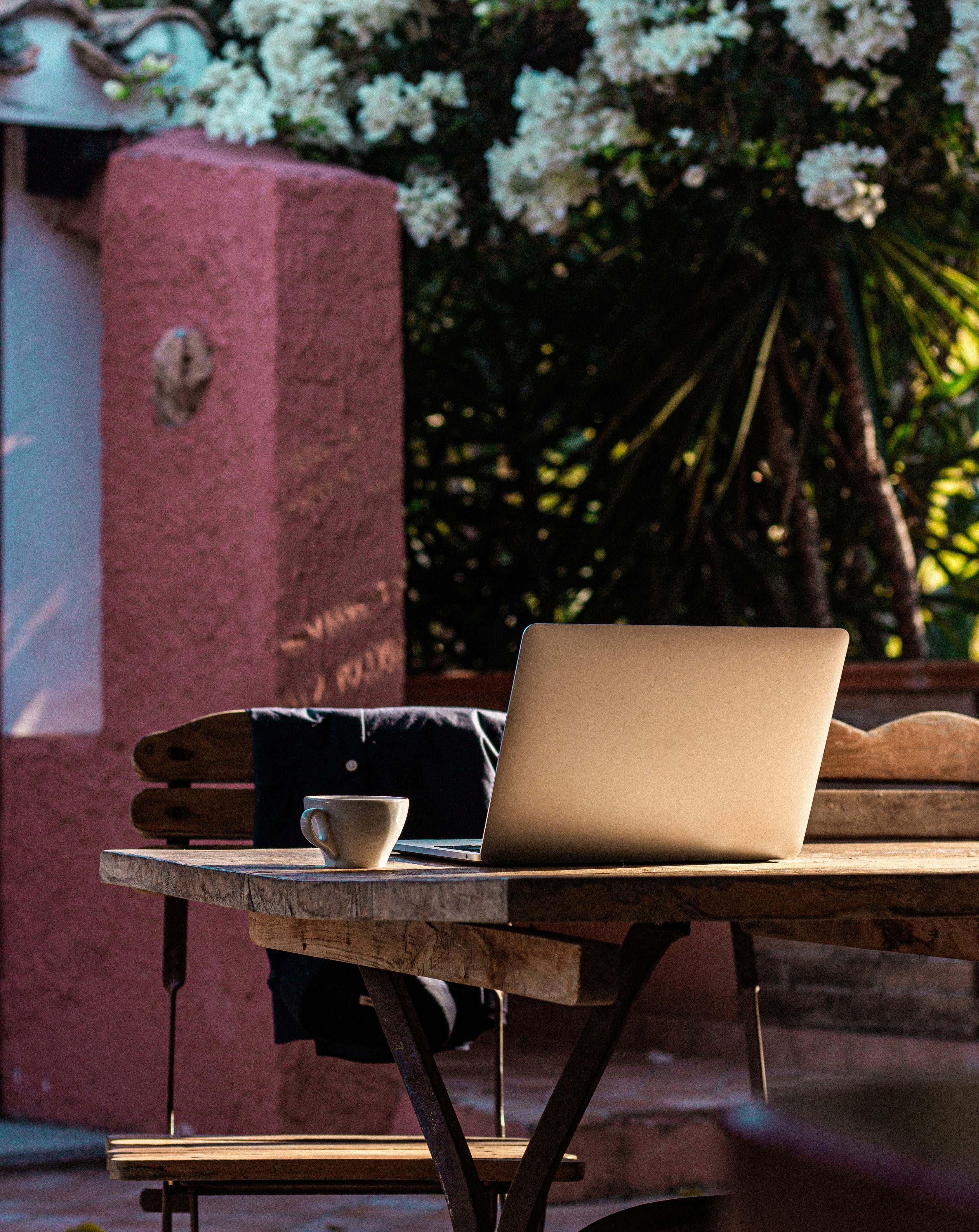 Bærbar computer og kaffe på en café eller på et hotel i et stille udendørs miljø. Billede, der illustrerer bleisure, fjernarbejde og fleksibiliteten til at kombinere arbejde med ferie.
