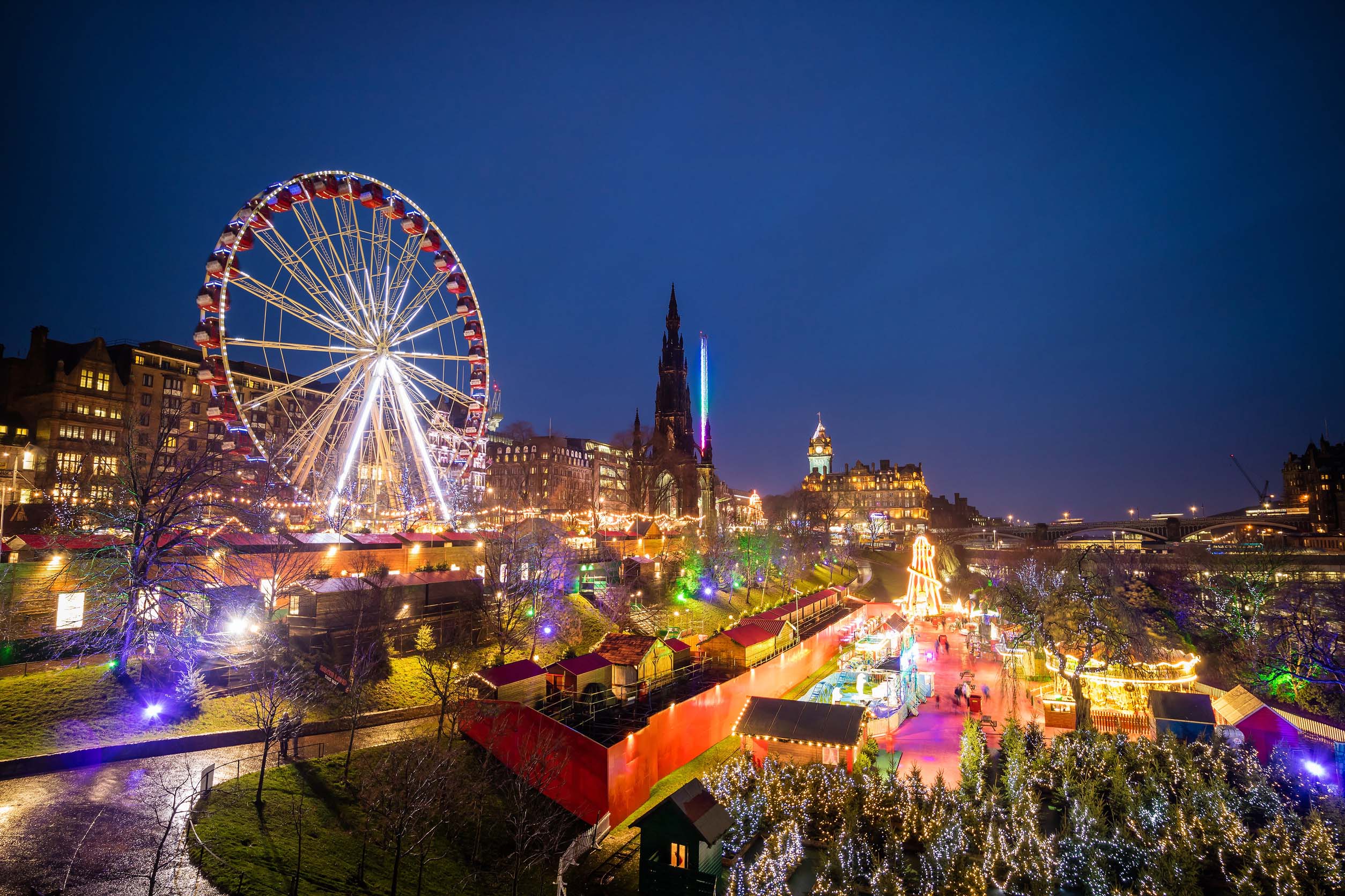 Edinburgh Christmas Market at night with a large illuminated Ferris wheel and festive lights in the city centre.
