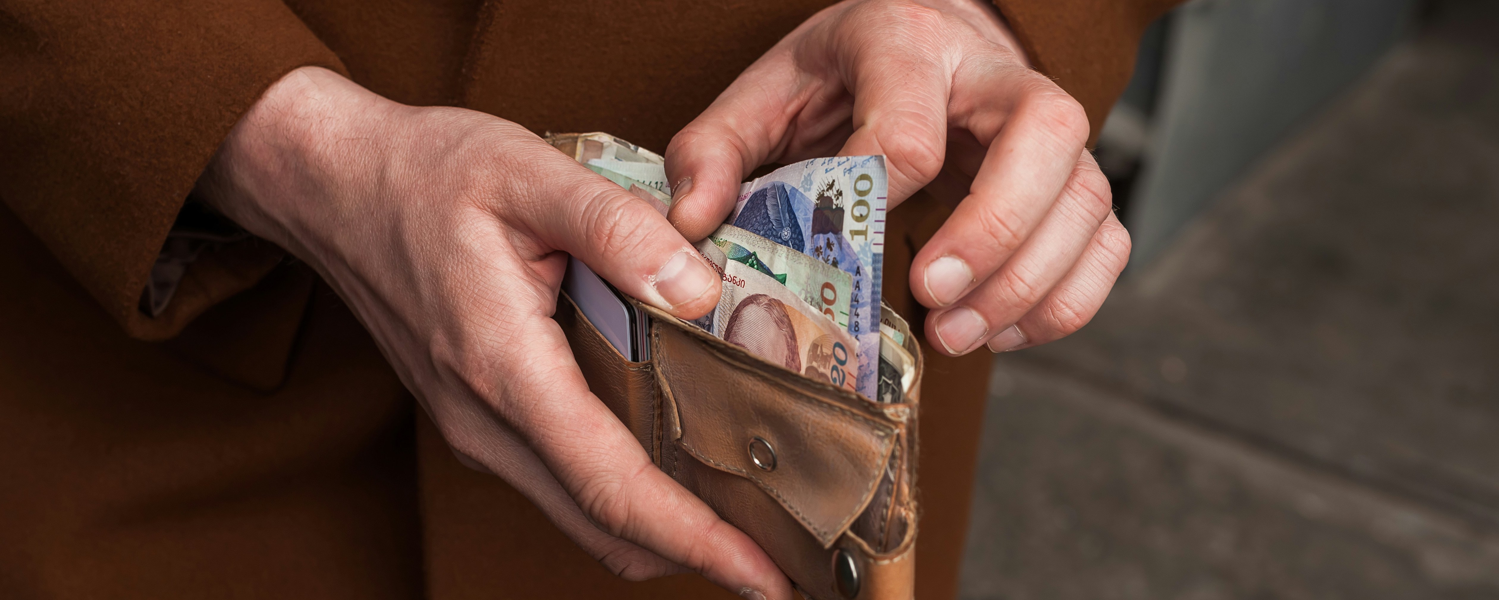 Personen åbner en pung fyldt med svenske pengesedler, inklusive 500-kroners sedler, udendørs.