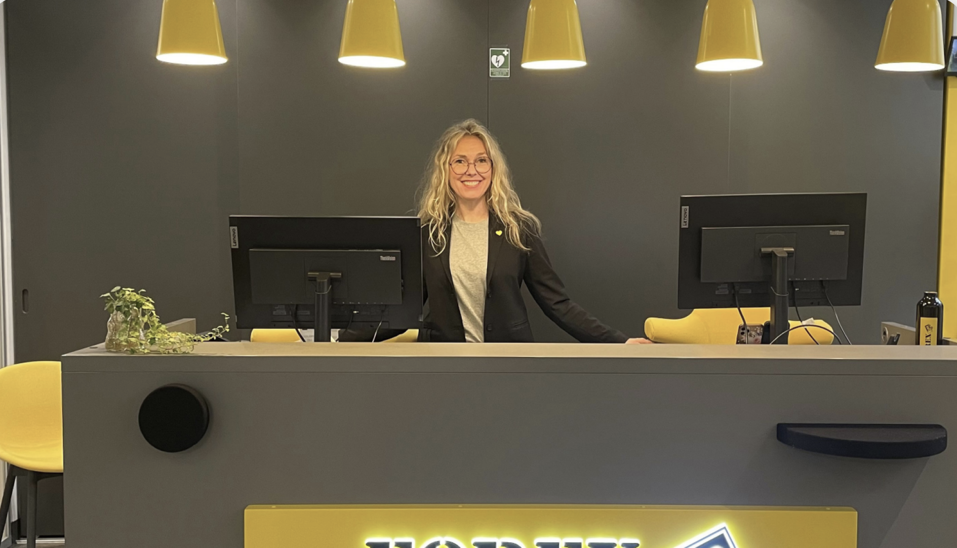 Receptionist foran moderne receptionsdisk med gule lamper og kontorstole