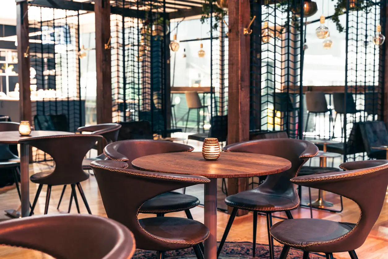 Loungeomr&aring;de med runda tr&auml;bord och m&ouml;rka stoppade stolar, mjuk belysning och dekorativa lampor i en modern inomhusmilj&ouml;.