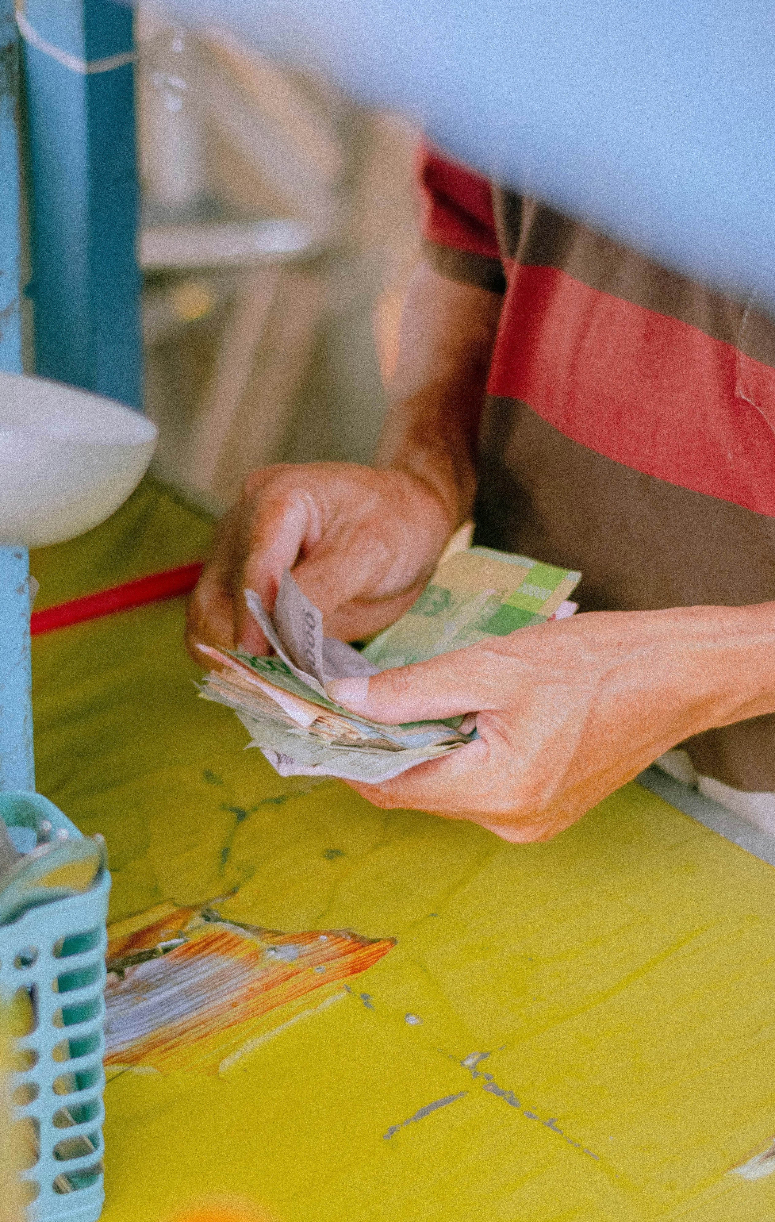 Person, der tæller kontanter ved en farverig madbod, omgivet af bestik, saucer og køkkenudstyr.