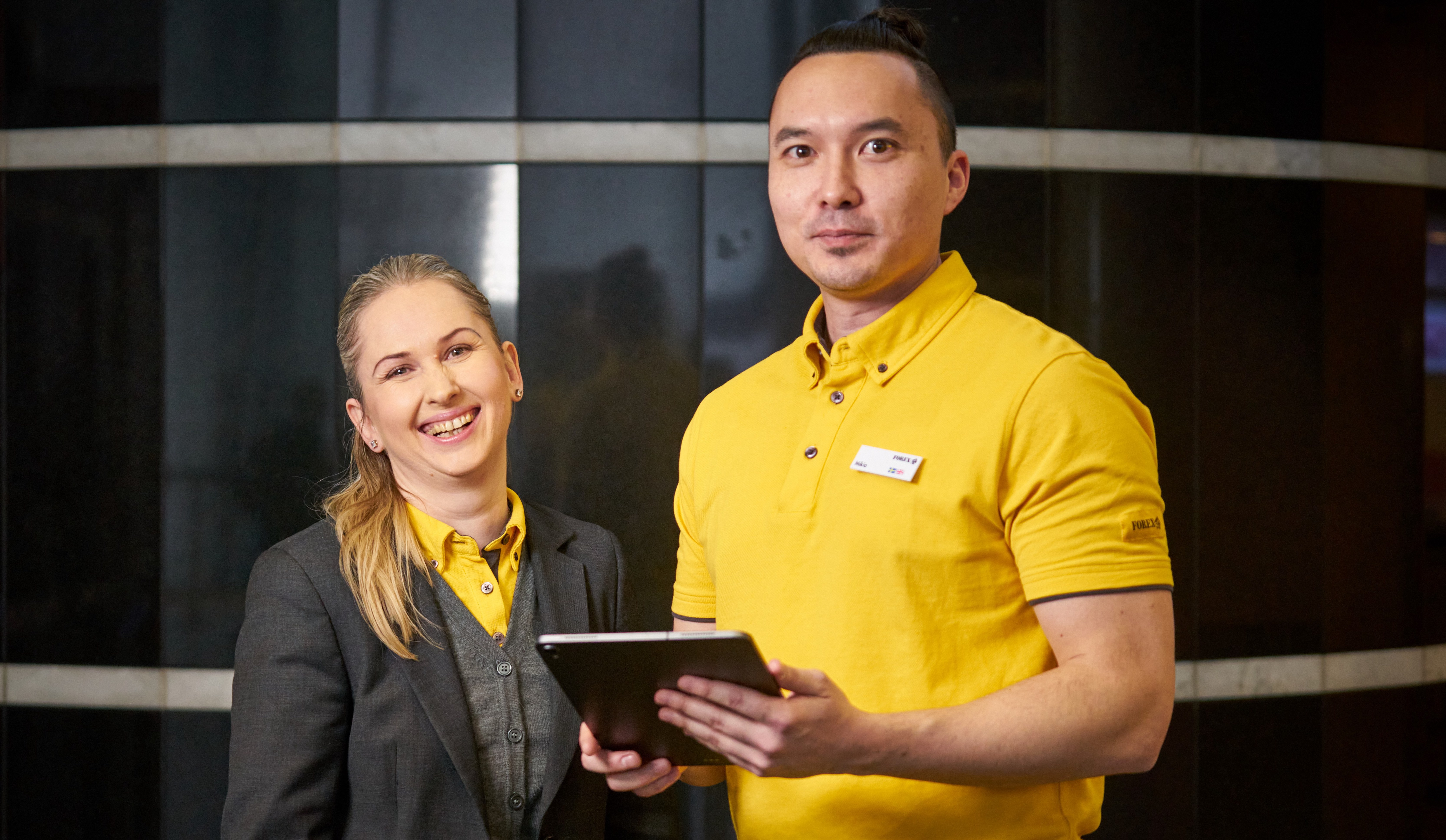 FOREX-medarbejdere i en valutavekslingsbutik med en tablet, iført FOREX-arbejdsuniformer.