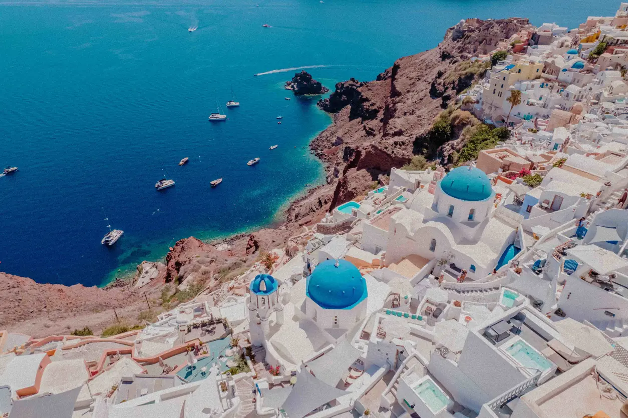 Panoramautsikt över Santorini med vita byggnader, blå kupoler och kristallklart hav. Ikonisk grekisk ö i Kykladerna.