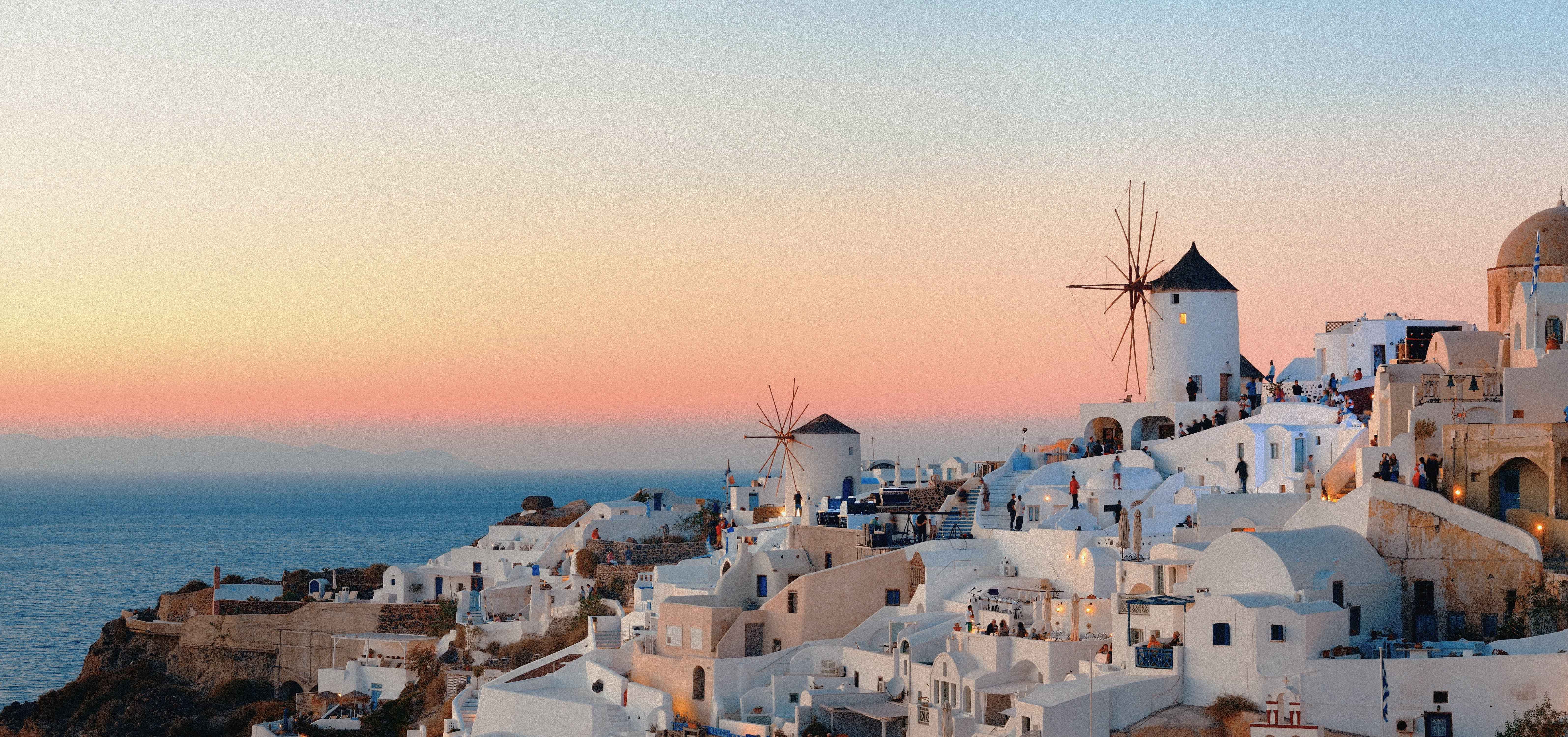 Whitewashed houses and classic windmills in Oia, Santorini during sunset. Romantic view of the Aegean Sea in Greece.