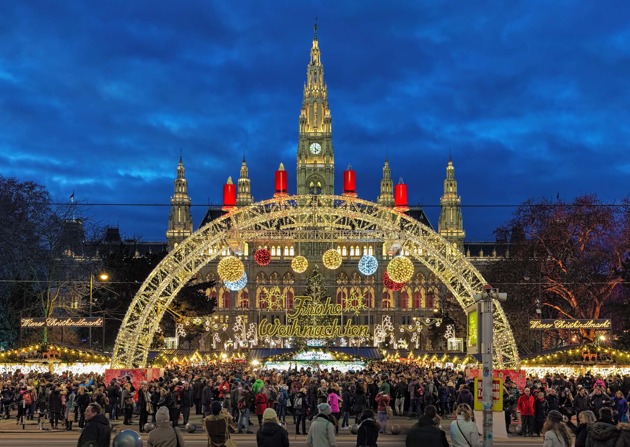 Crowds enjoying the Vienna Christmas Market at Rathausplatz with illuminated arches, decorations, and the city hall in the background.