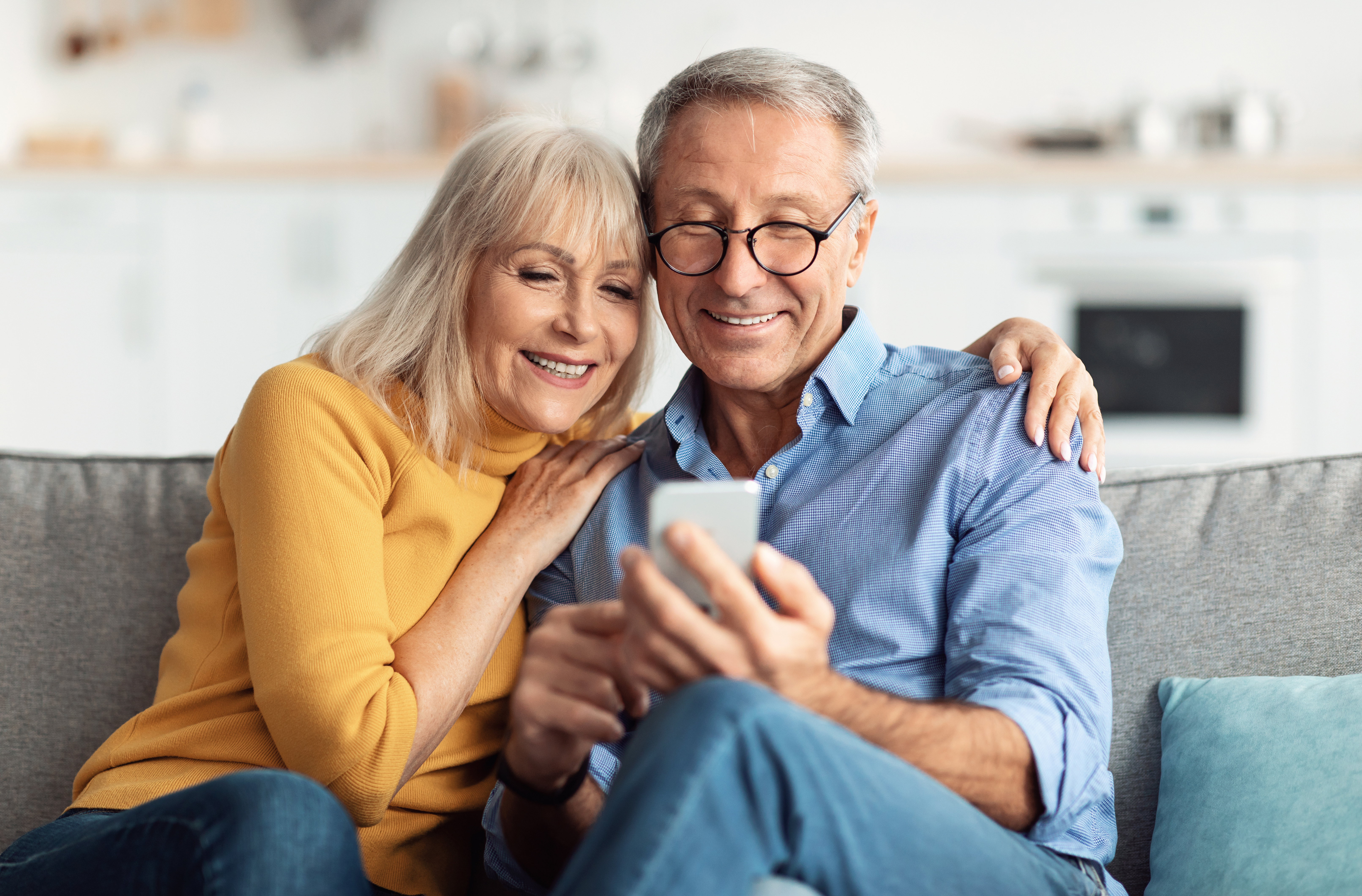 Elderly couples sit together on the couch and happily look at a smartphone.