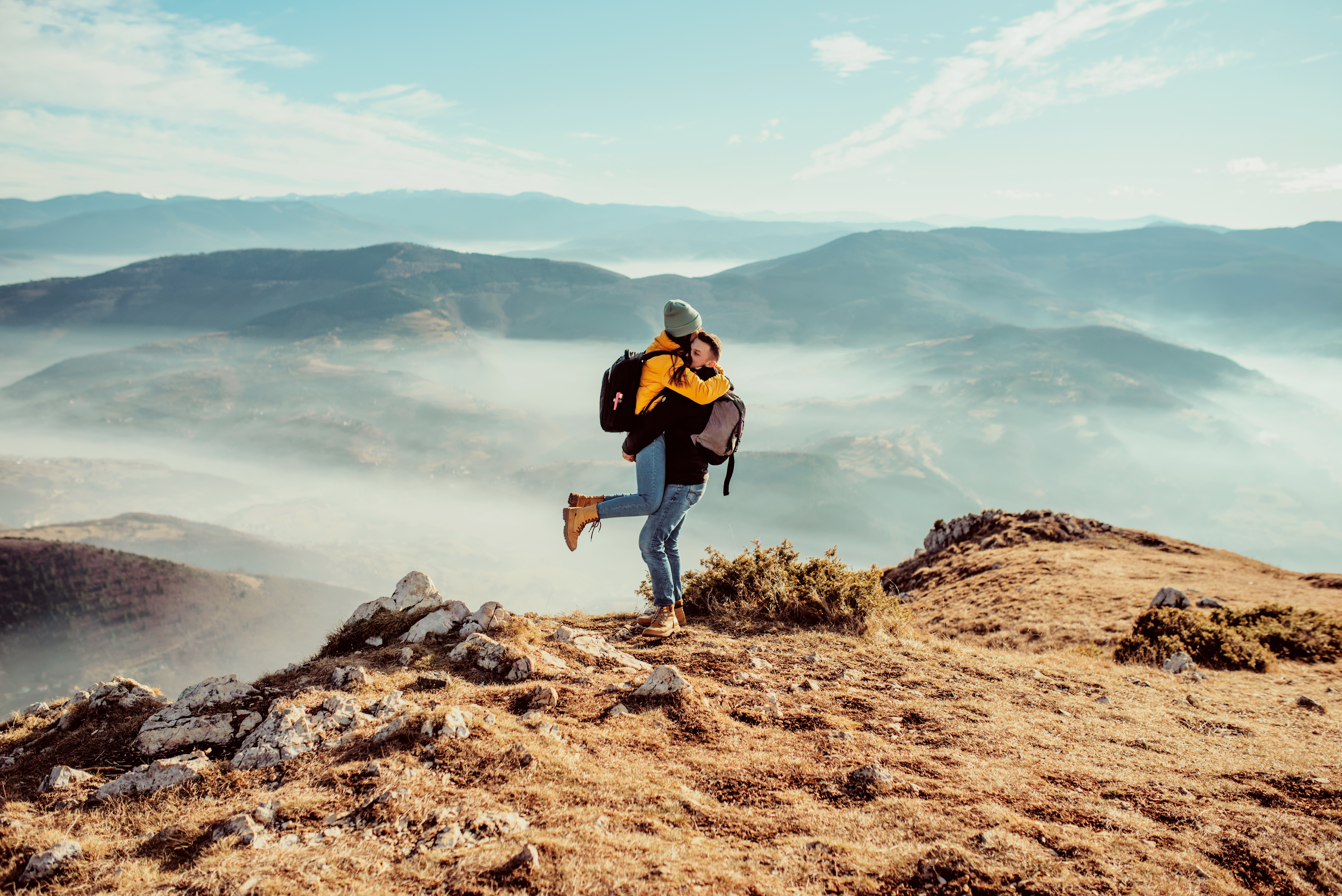 Couples embrace each other on a mountaintop with misty valleys in the background.