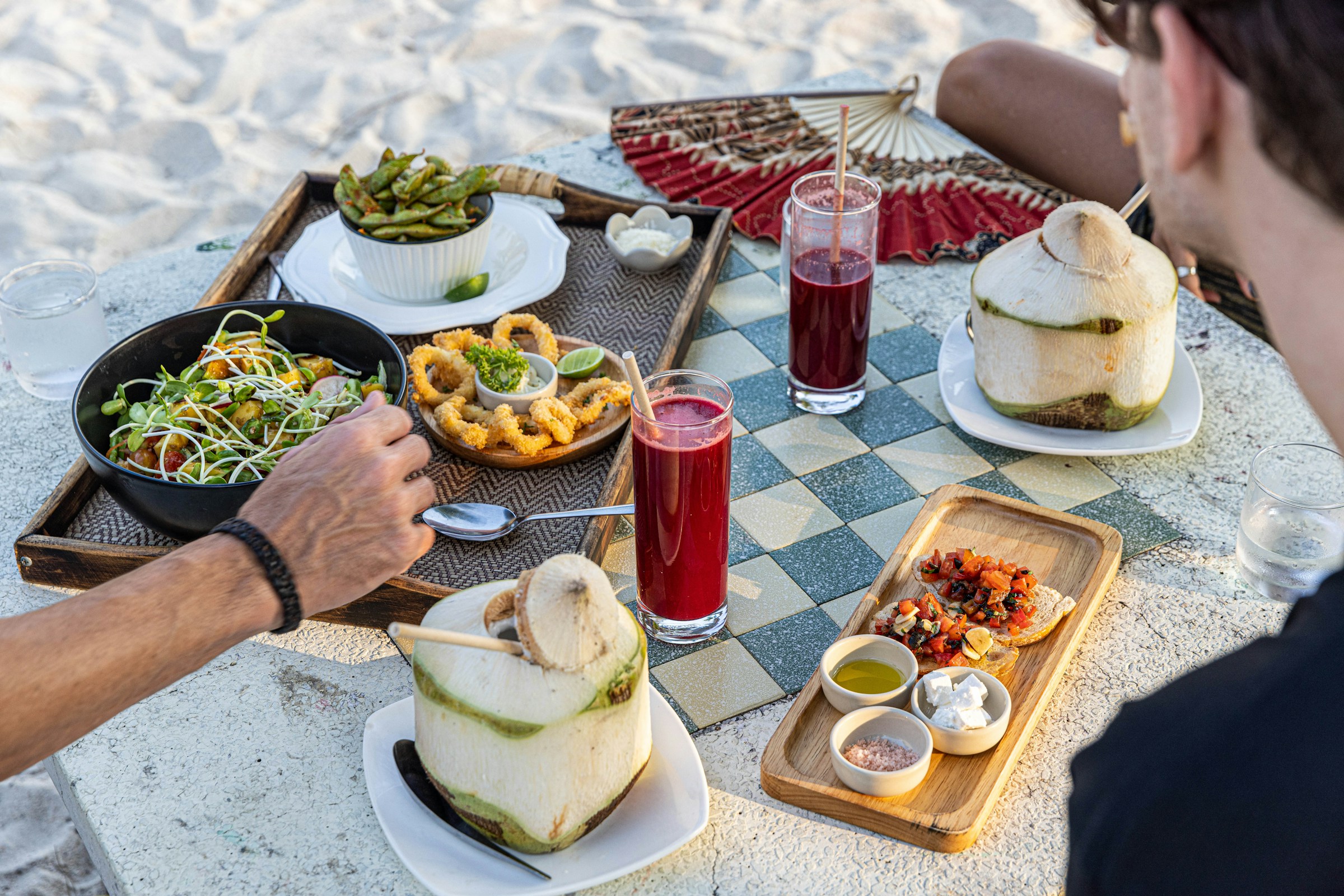 Beach picnic with coconut drinks, tropical salads, and appetizers on a checkered table.
