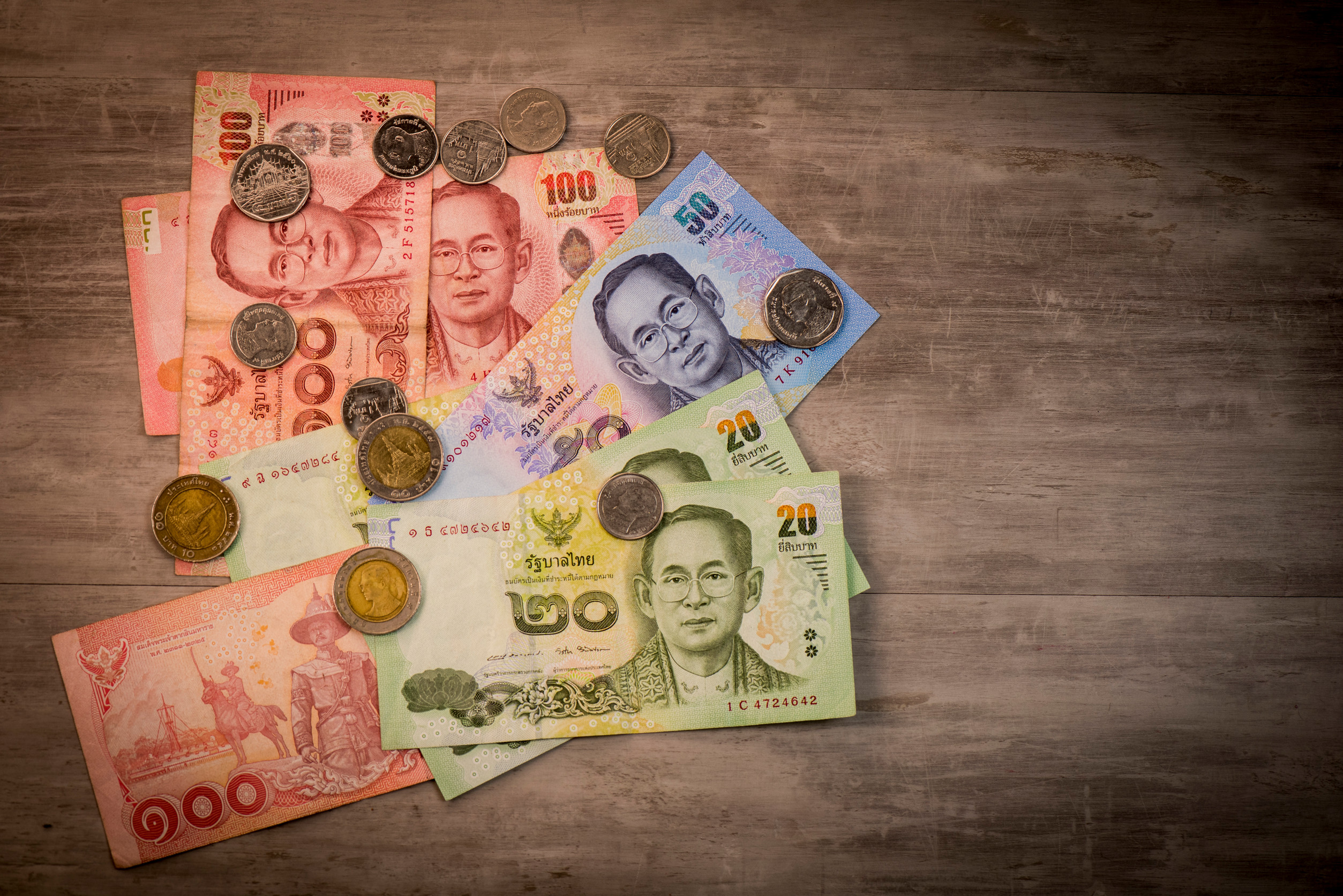 Thai baht notes and coins scattered on a wooden floor.