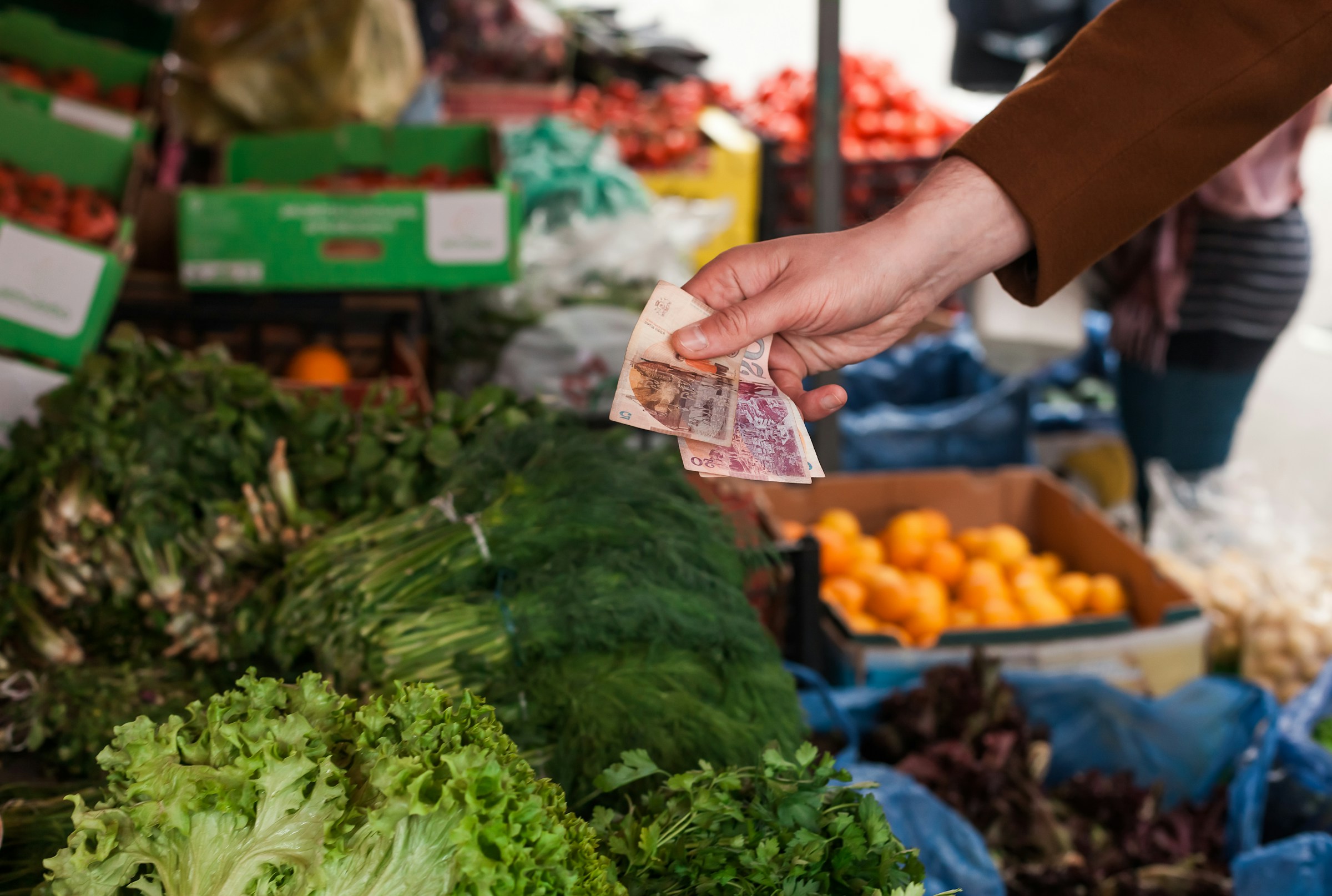 Person køber grøntsager på et udendørs marked og beholder penge over friske salathoveder og andre grøntsager i Sverige.