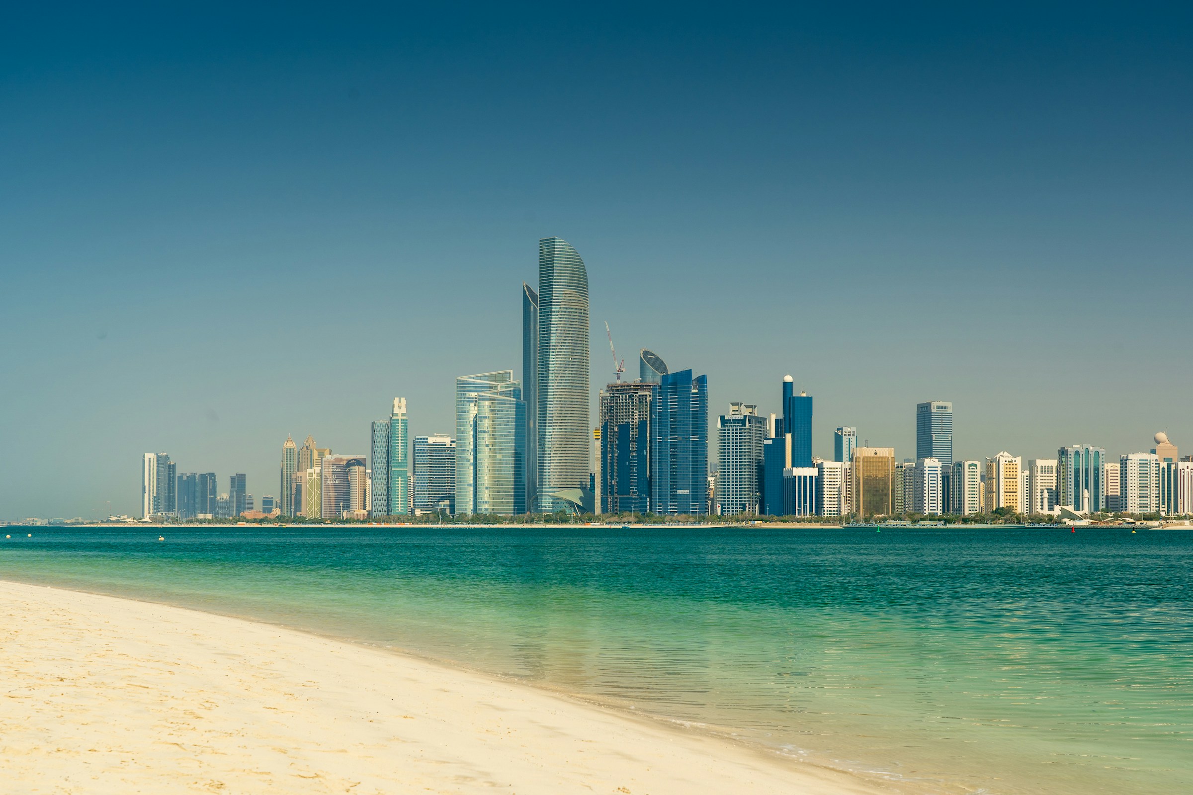 Abu Dhabi skyline featuring modern skyscrapers with a clear blue sky and a sandy beach in the foreground.