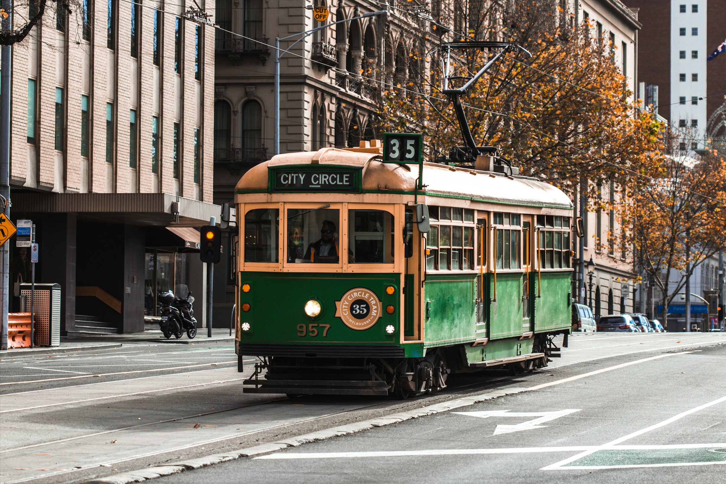 Historic green City Circle tram number 957 in downtown, surrounded by urban architecture and autumn trees.