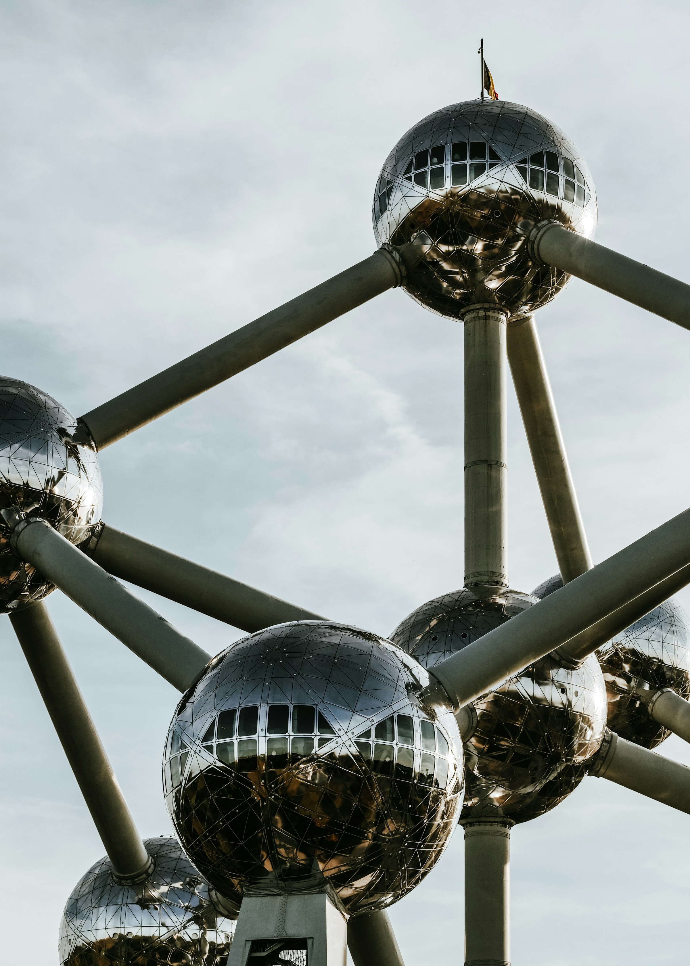 Close-up of the Atomium in Brussels, showcasing its metallic spheres and connecting tubes against a cloudy sky.