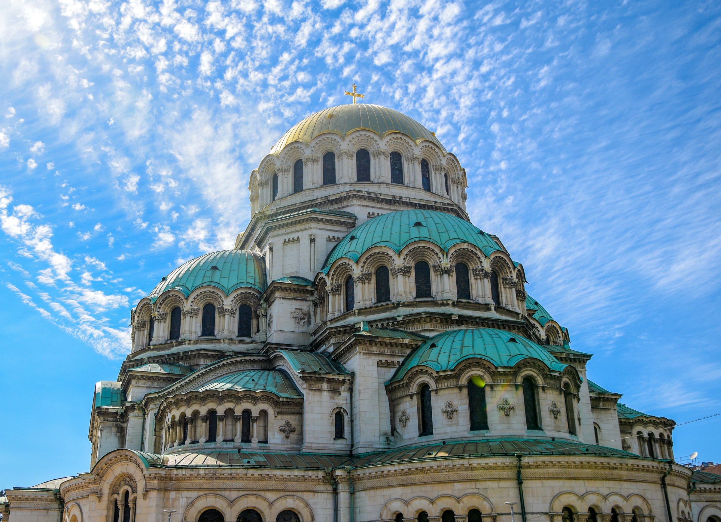Alexander Nevsky Cathedral in Sofia, Bulgaria, showcasing its iconic green domes against a vibrant blue sky with scattered clouds.