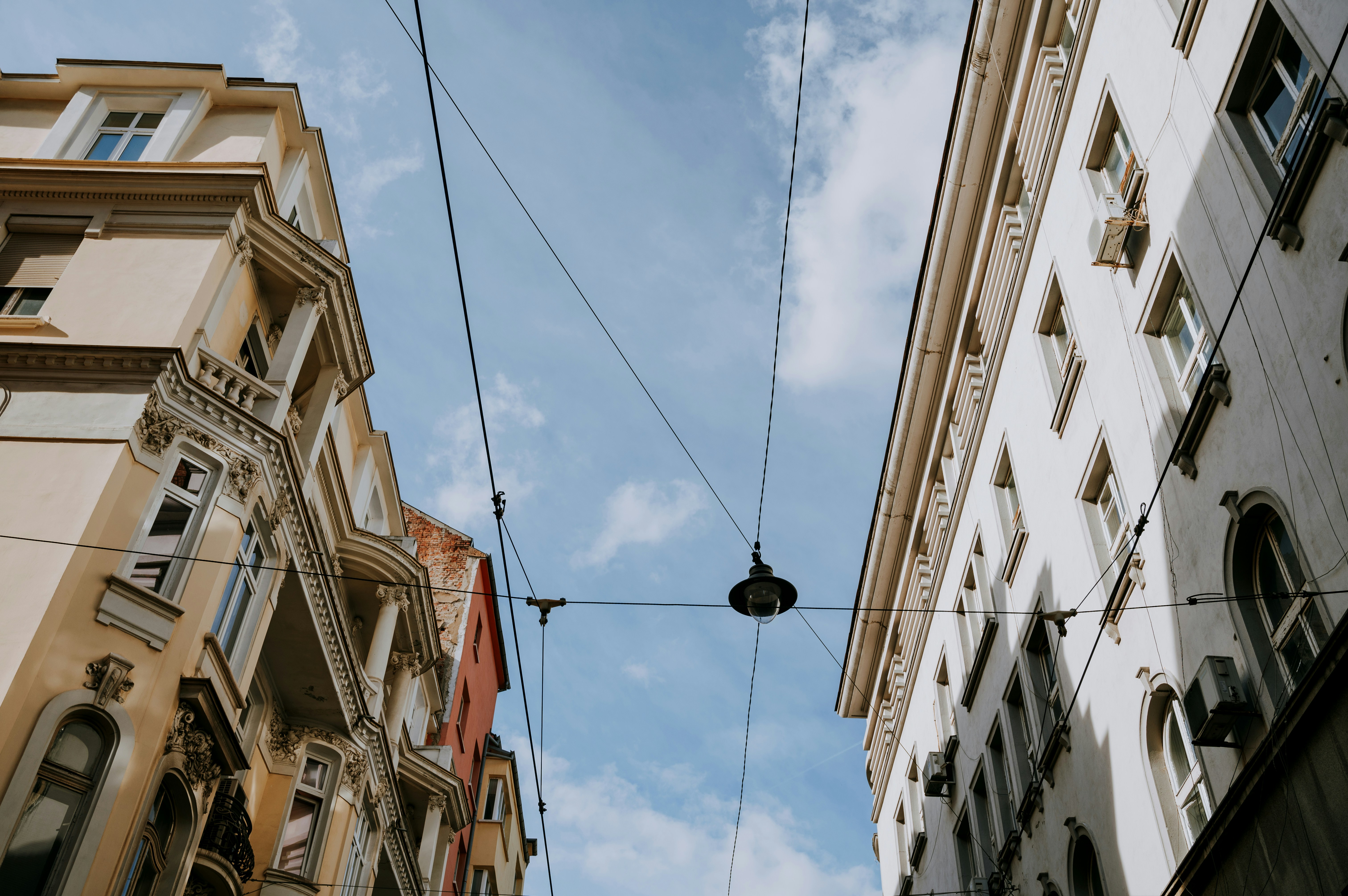 Historiske bygninger mod en blå himmel med elektriske ledninger i forgrunden, set opad fra gadeniveau