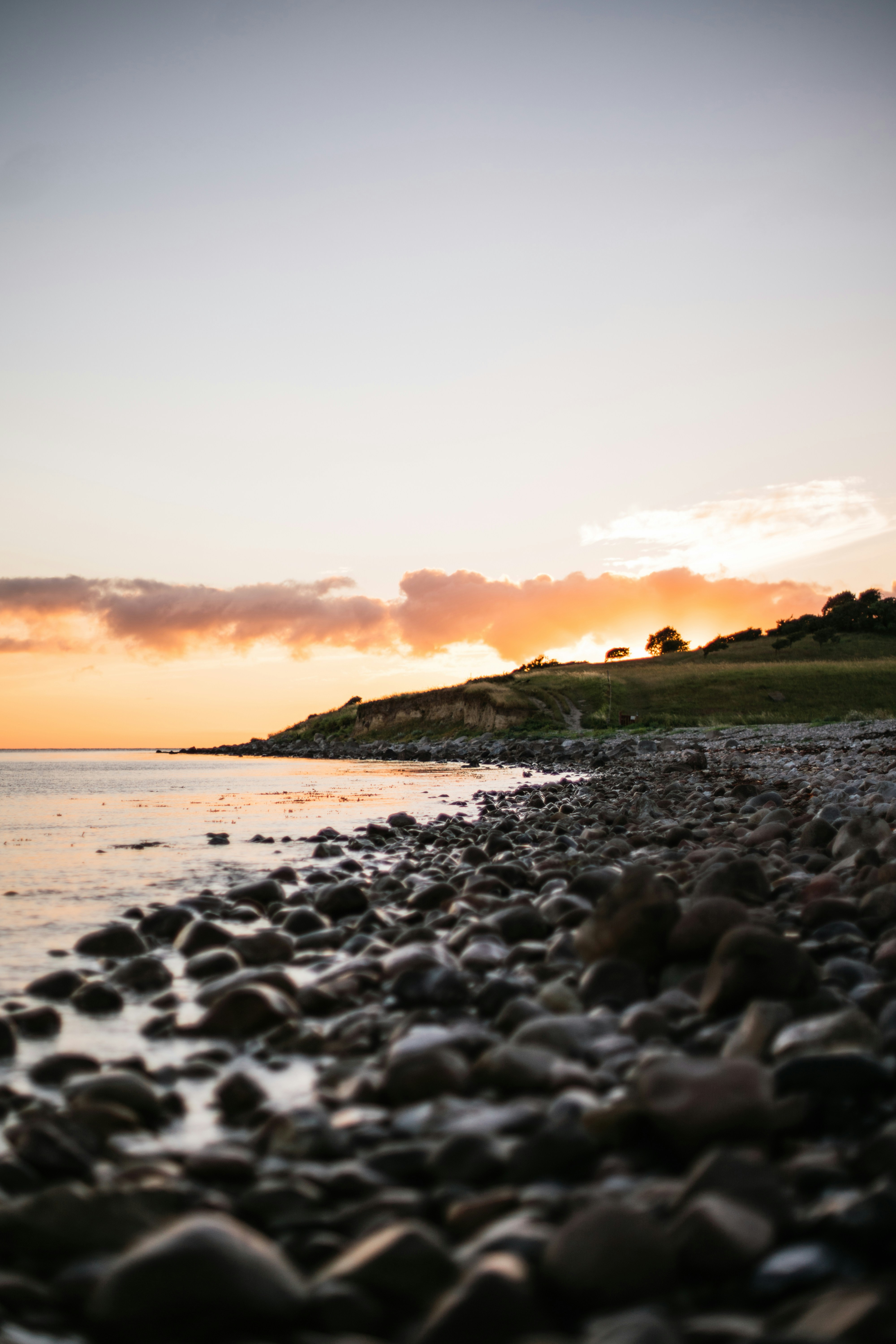 Solnedgang over stenstrand ved havet med kystlinje i baggrunden, Danmark