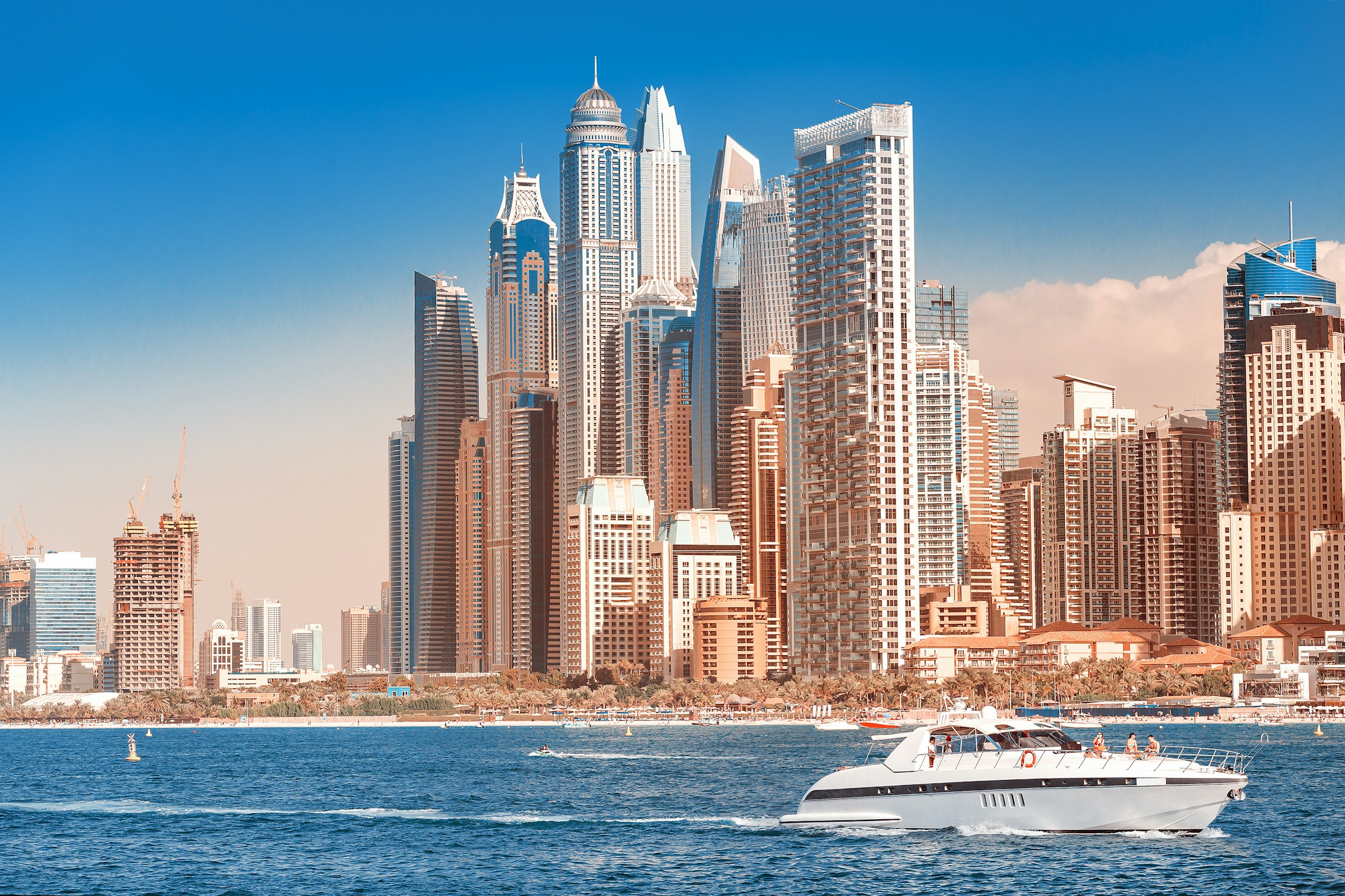 Dubai Marina skyline with modern skyscrapers and a yacht sailing in the blue water.