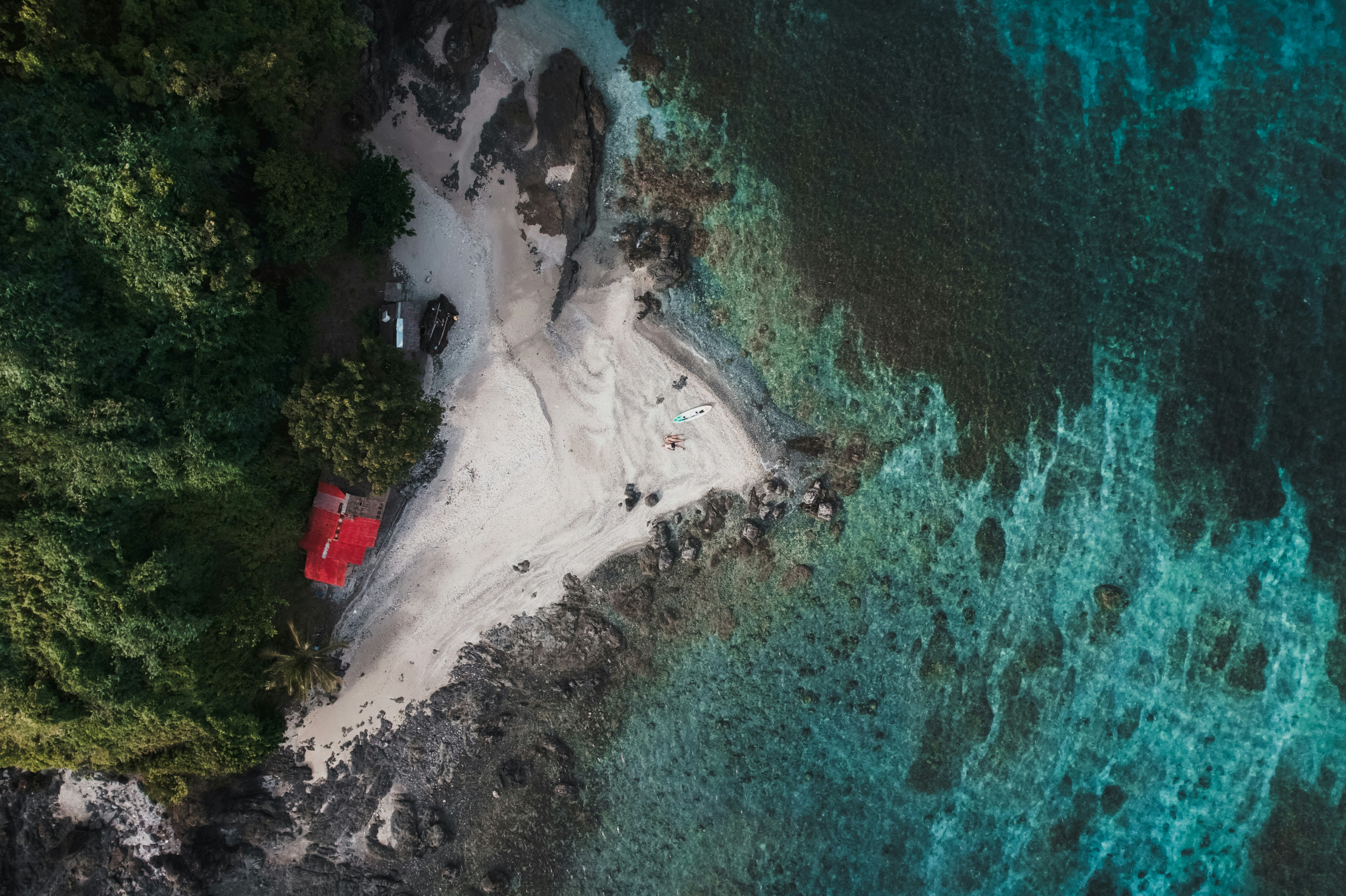Luftfoto af en isoleret strand med en rød bygning omgivet af frodig vegetation og klart, turkisblåt vand