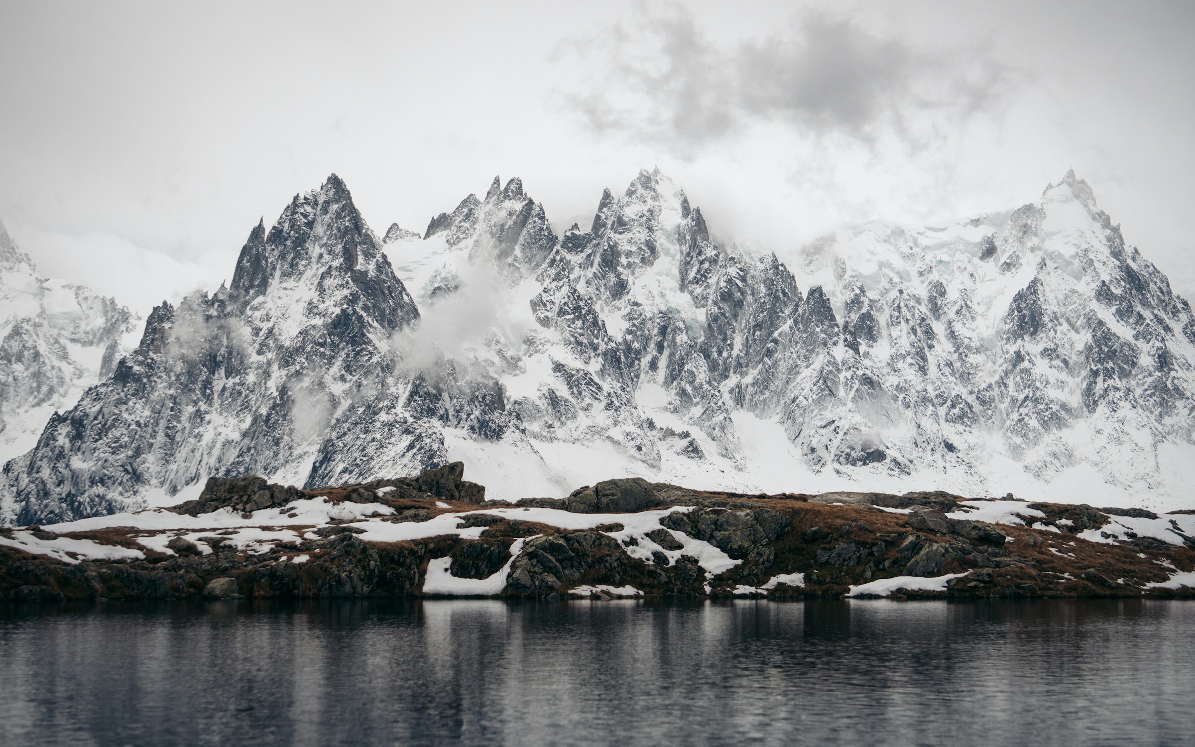 Sø ved foden af et mægtigt sneklædt bjerg mod en hvid himmel i Chamonix, Frankrig
