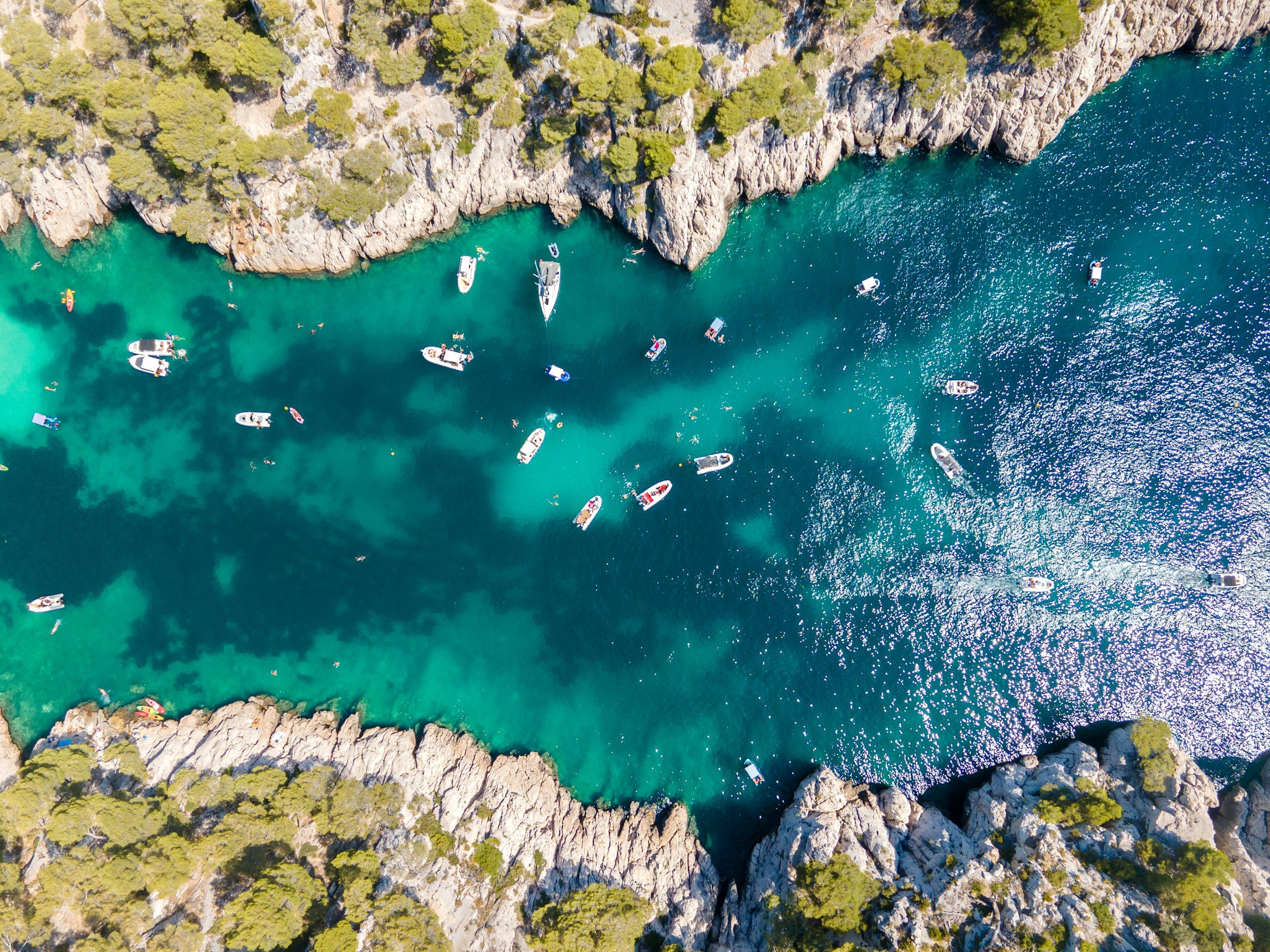 Aerial view of turquoise water surrounded by rocky cliffs with scattered boats and kayaks. Lush green trees line the coastline, creating a stunning natural landscape.