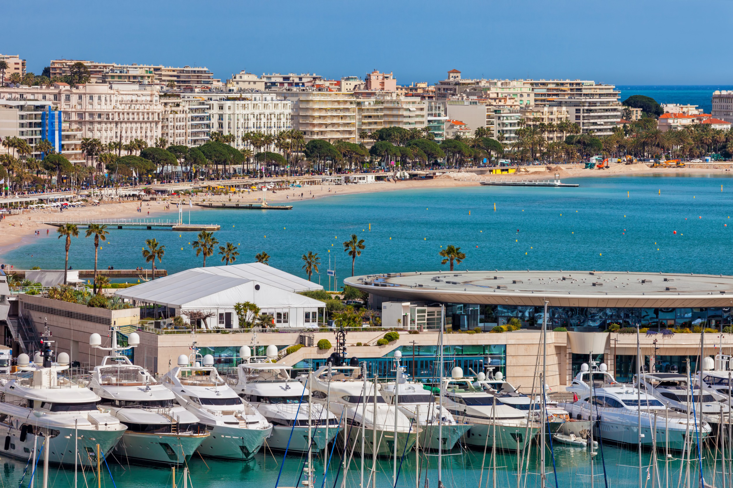 Havudsigt over Cannes Marina med luksusyachter i forgrunden og byens skyline i baggrunden under en klar blå himmel