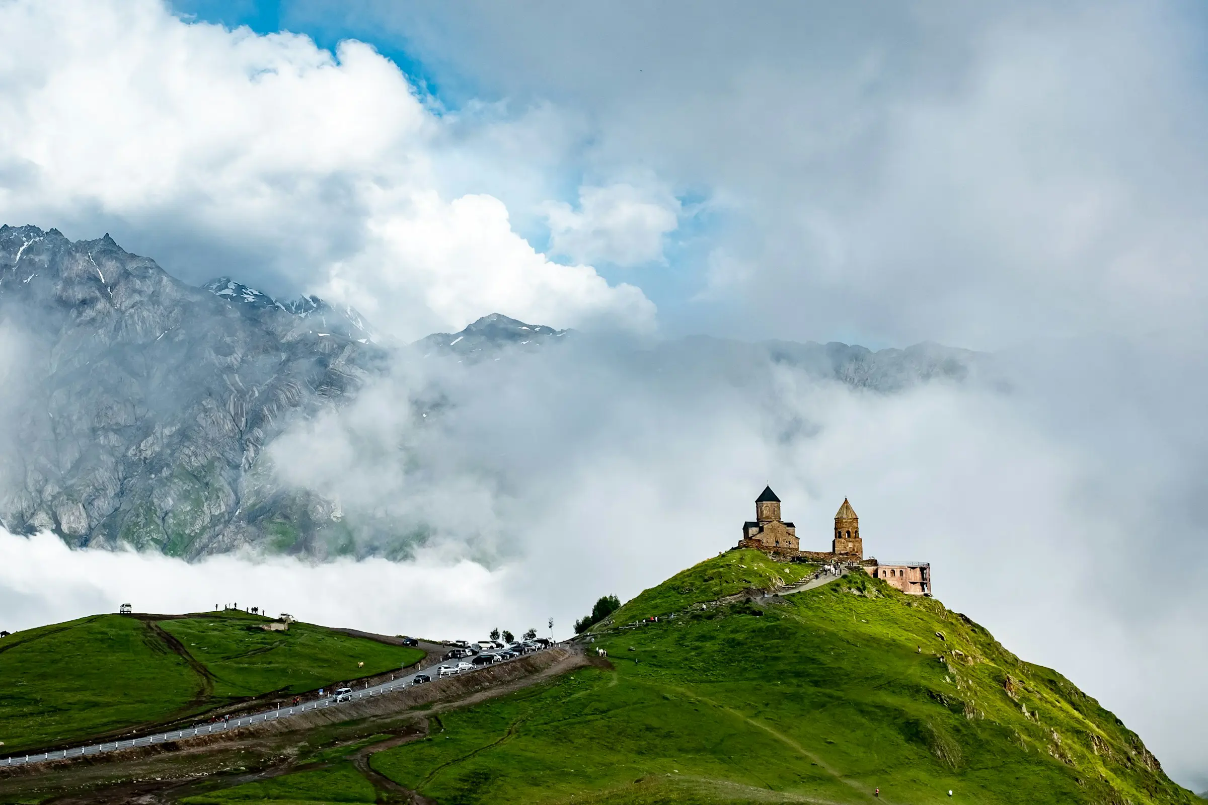 Kirke på en bjergtop omgivet af frodigt grønt landskab og tågeindhyllede bjerge i baggrunden af Georgia.
