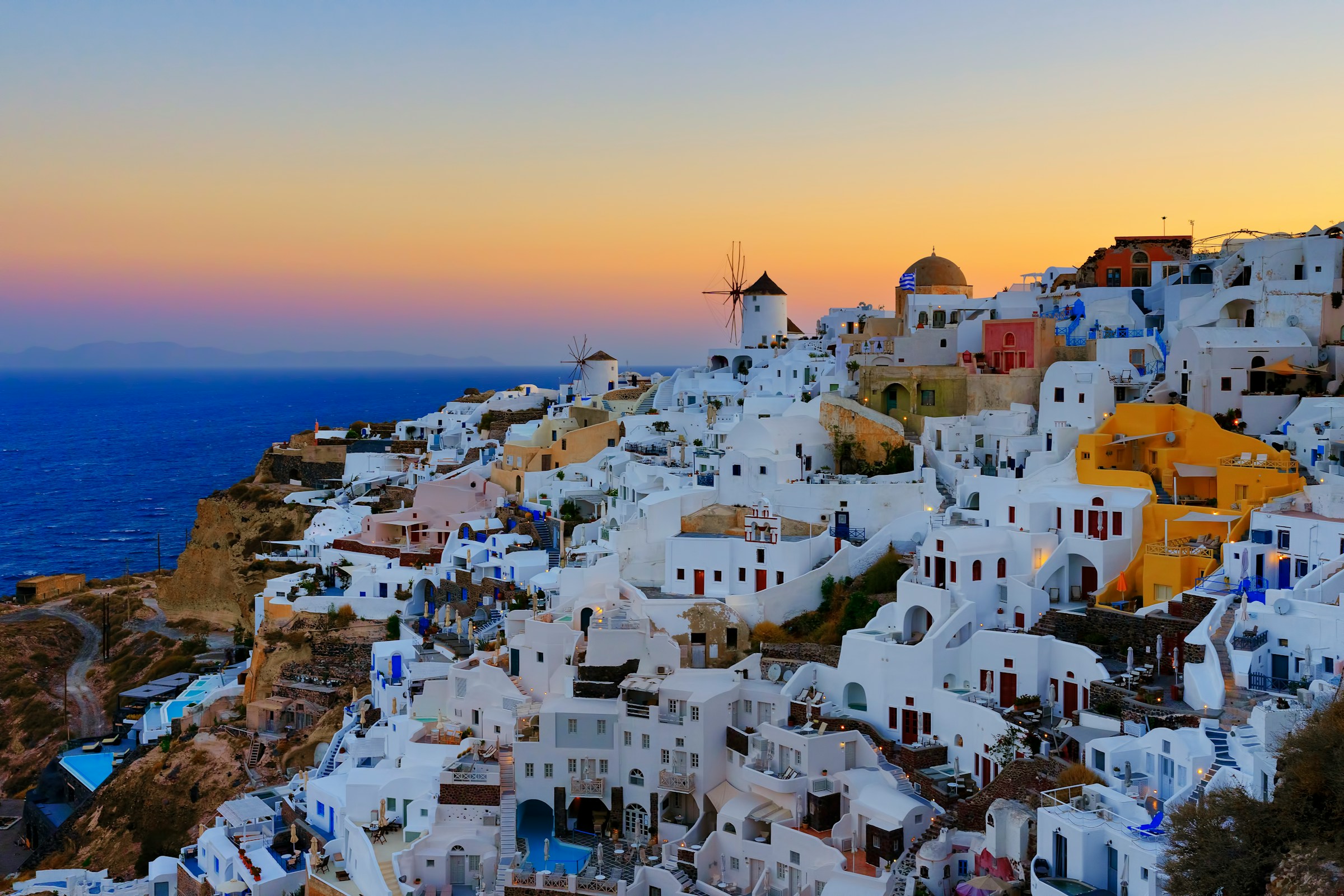 Solnedgang over Oia, Santorini i Grækenland: Hvide og pastelfarvede bygninger klynger sig til klippen med det glitrende blå hav i baggrunden