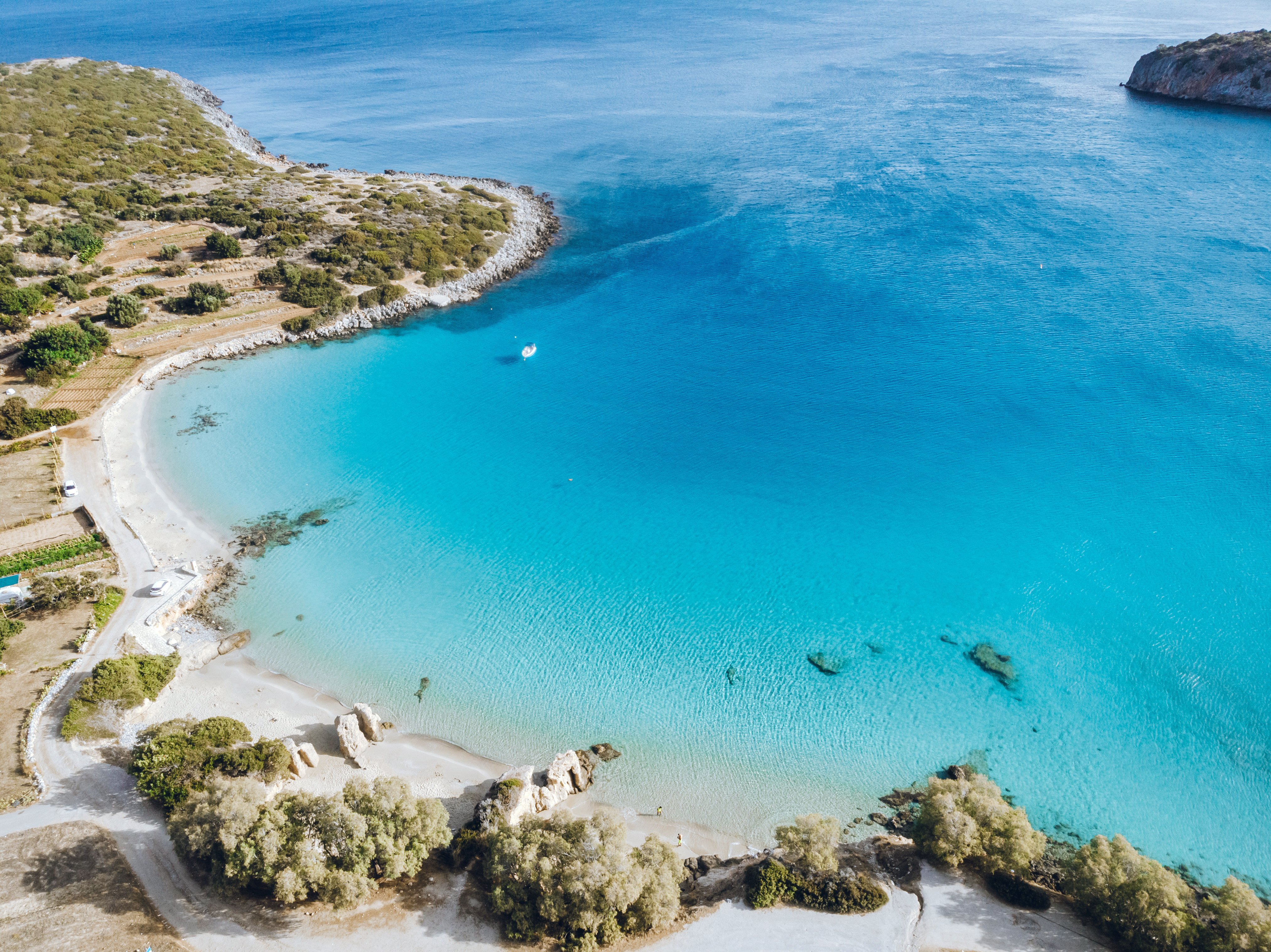 Flyfoto af en smuk strand med hvidt sand og turkisblåt hav omgivet af grøn bevoksning