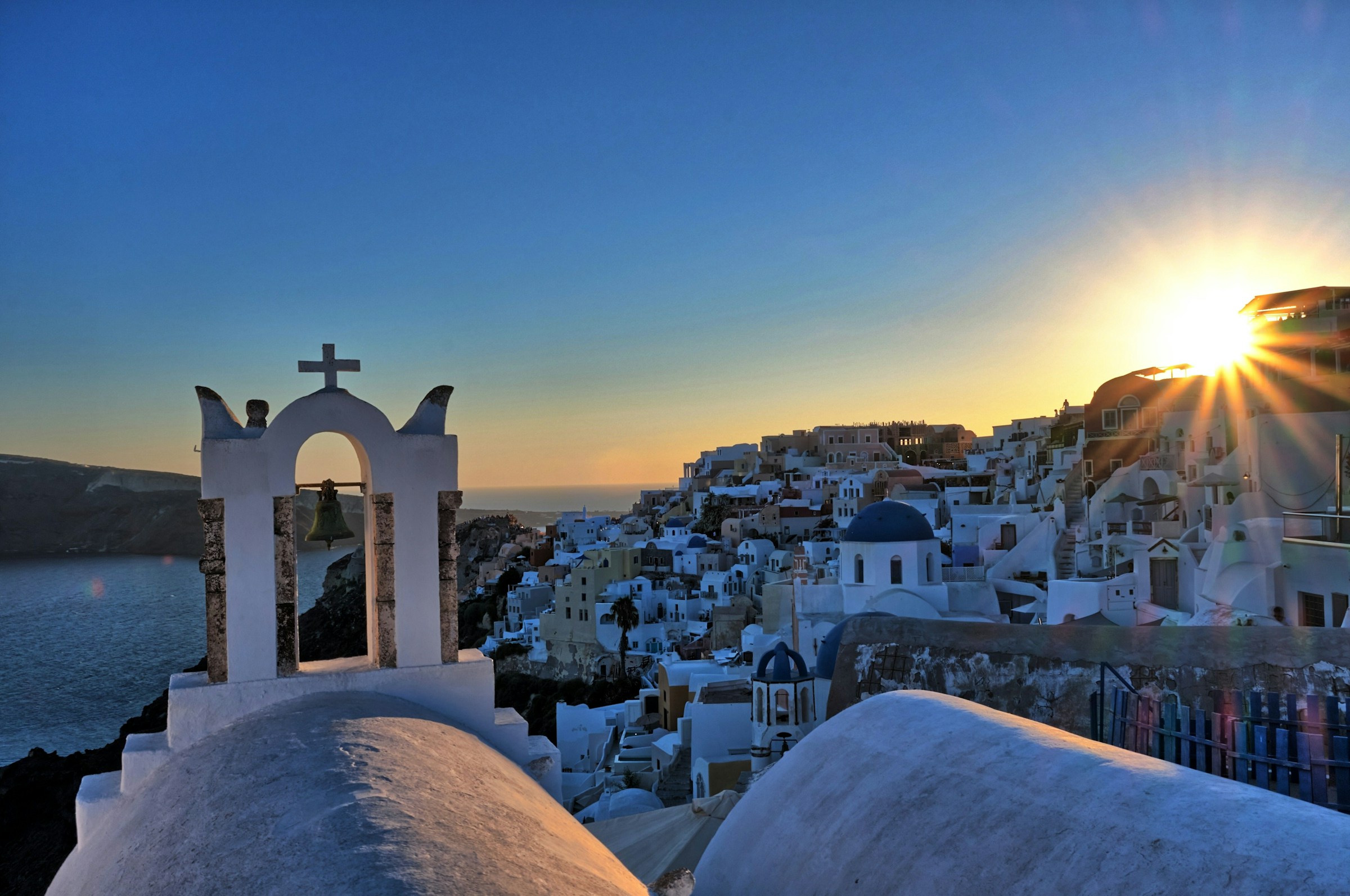 Solnedgang over Santorini, Grækenland med traditionelle hvide bygninger og blå kupler ved kysten