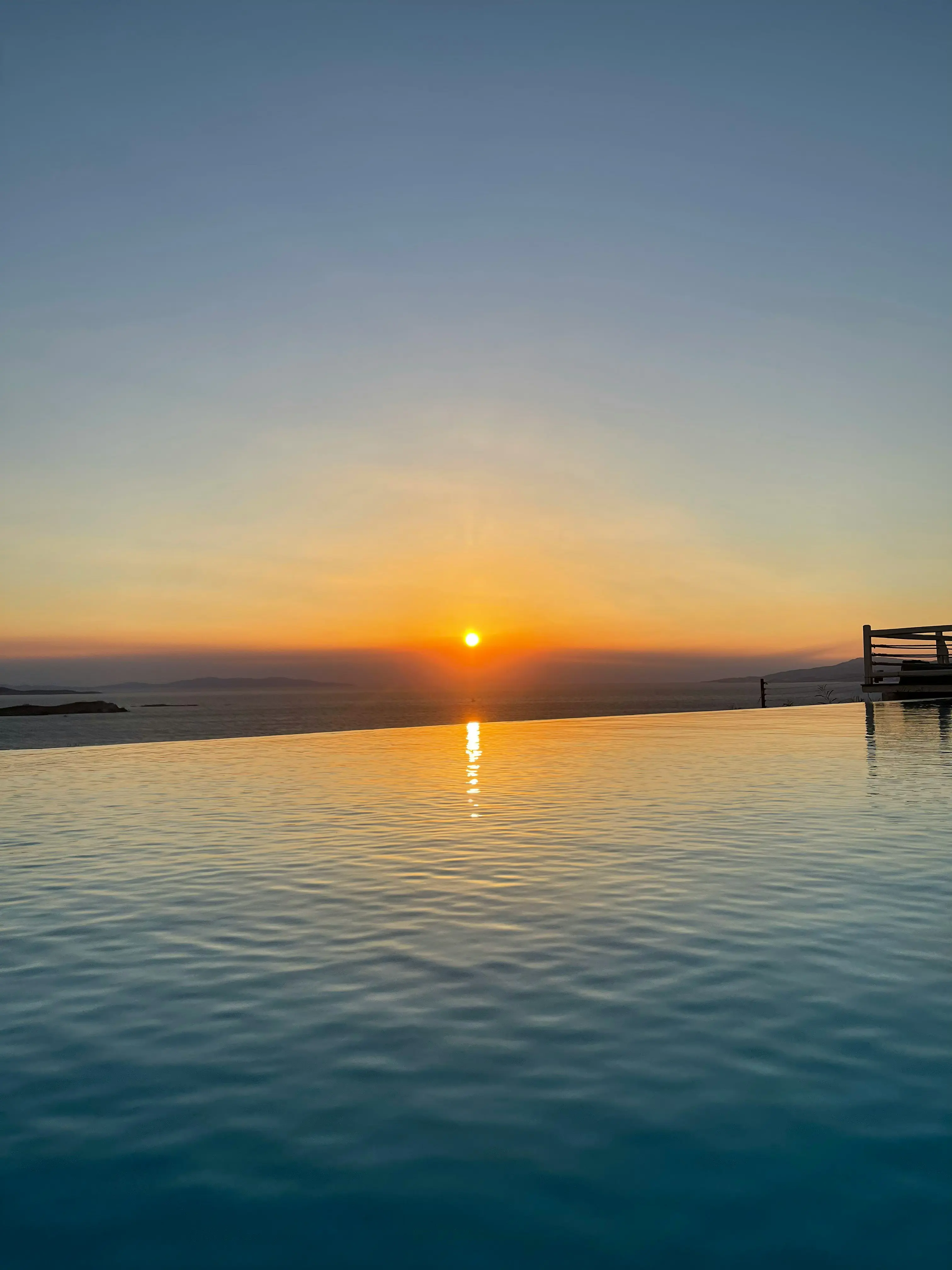Sunset view over an infinity pool with a calm ocean horizon in the distance, creating a serene and picturesque scene.