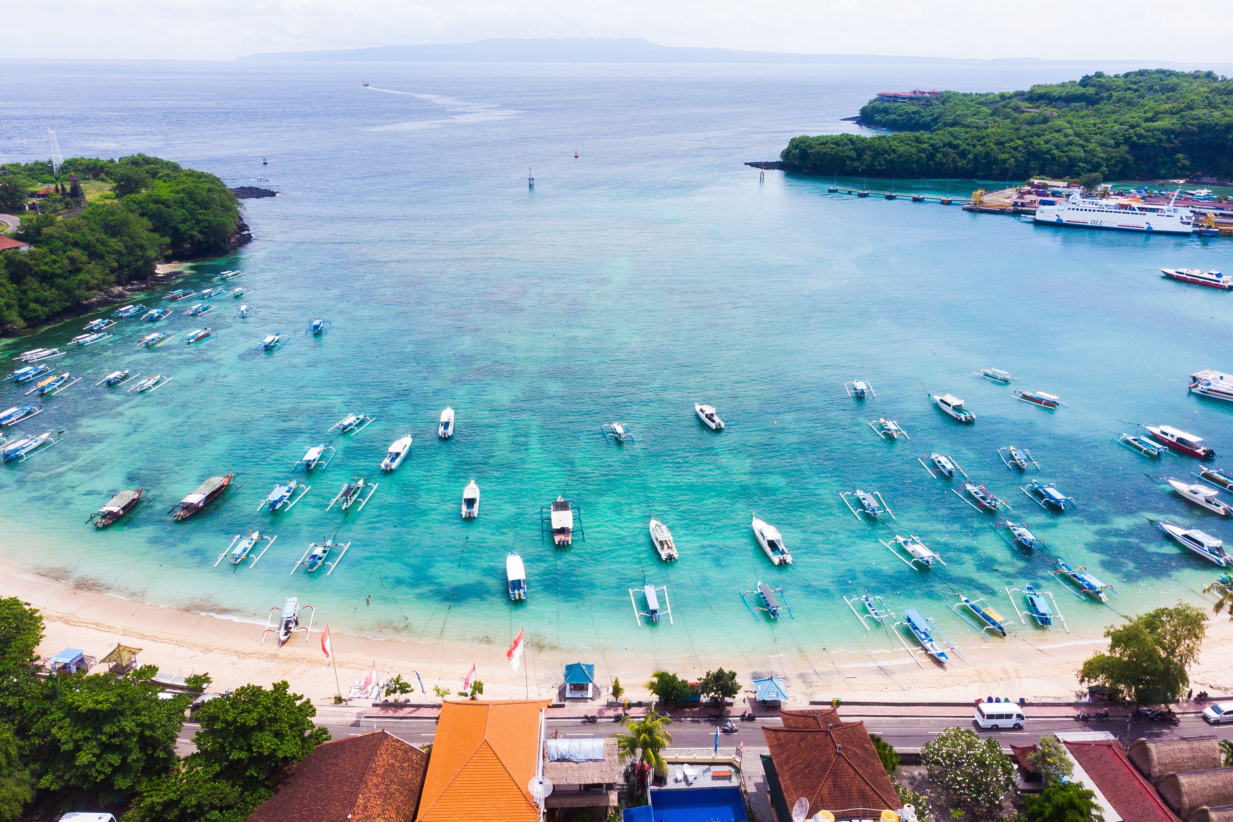 Luftfoto af tropisk kystlandskab med mange både i krystalklart vand nær en strand omgivet af frodig vegetation på øen Nusa Lembongan, Bali, Indonesien