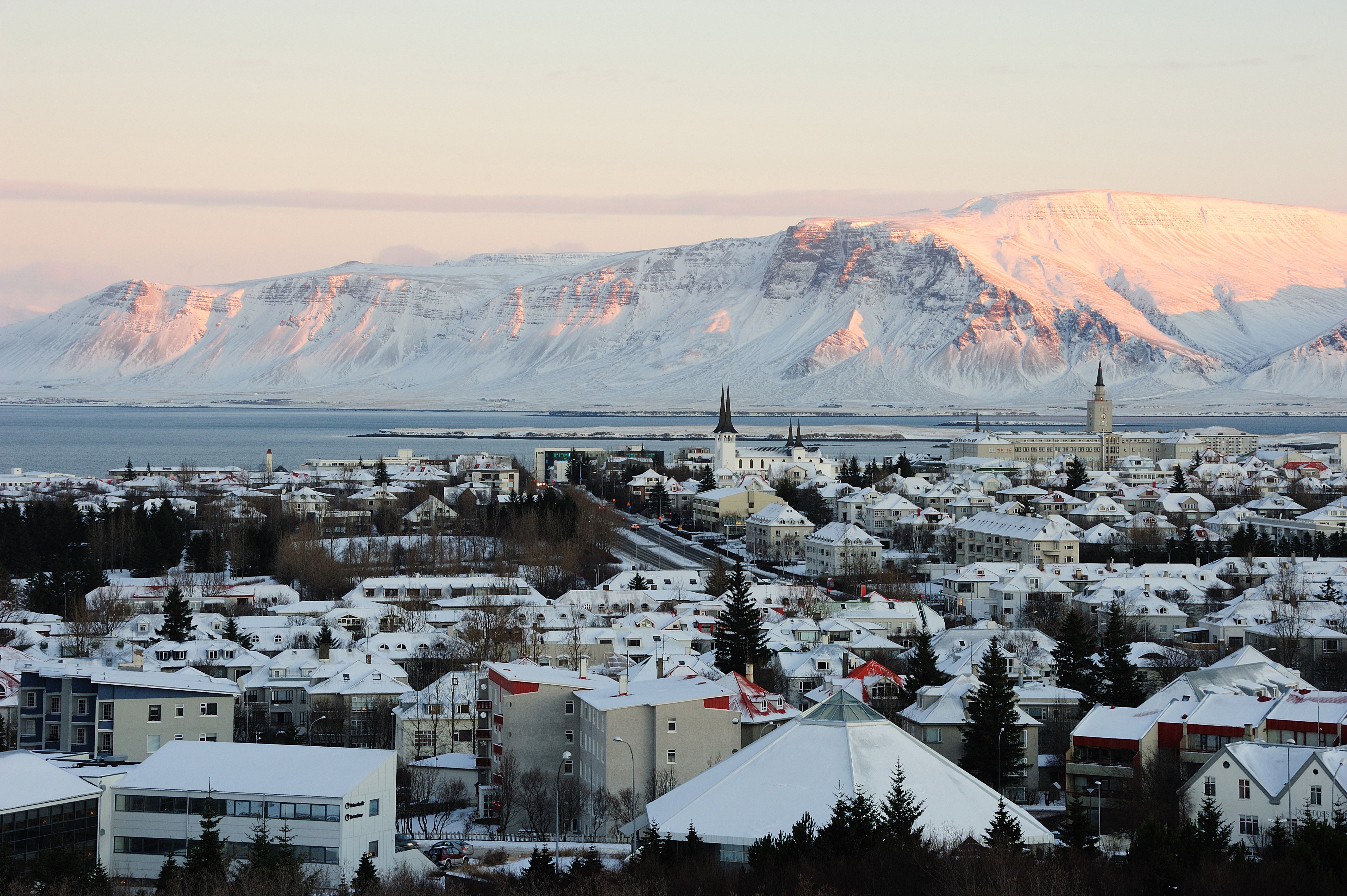 Udsigt over Reykjavik by med bjerge i baggrunden under en solnedgang