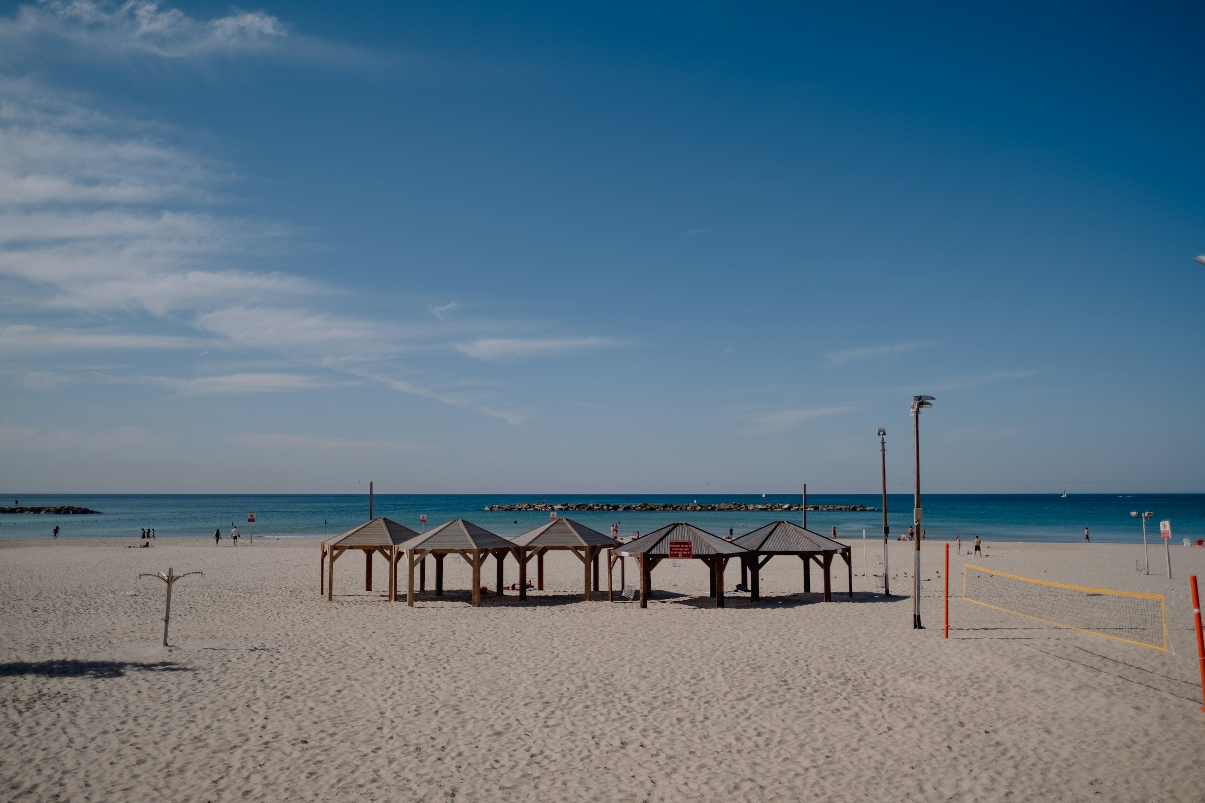 Beachfront view with wooden shelters on sandy shore, calm blue sea, and clear sky.