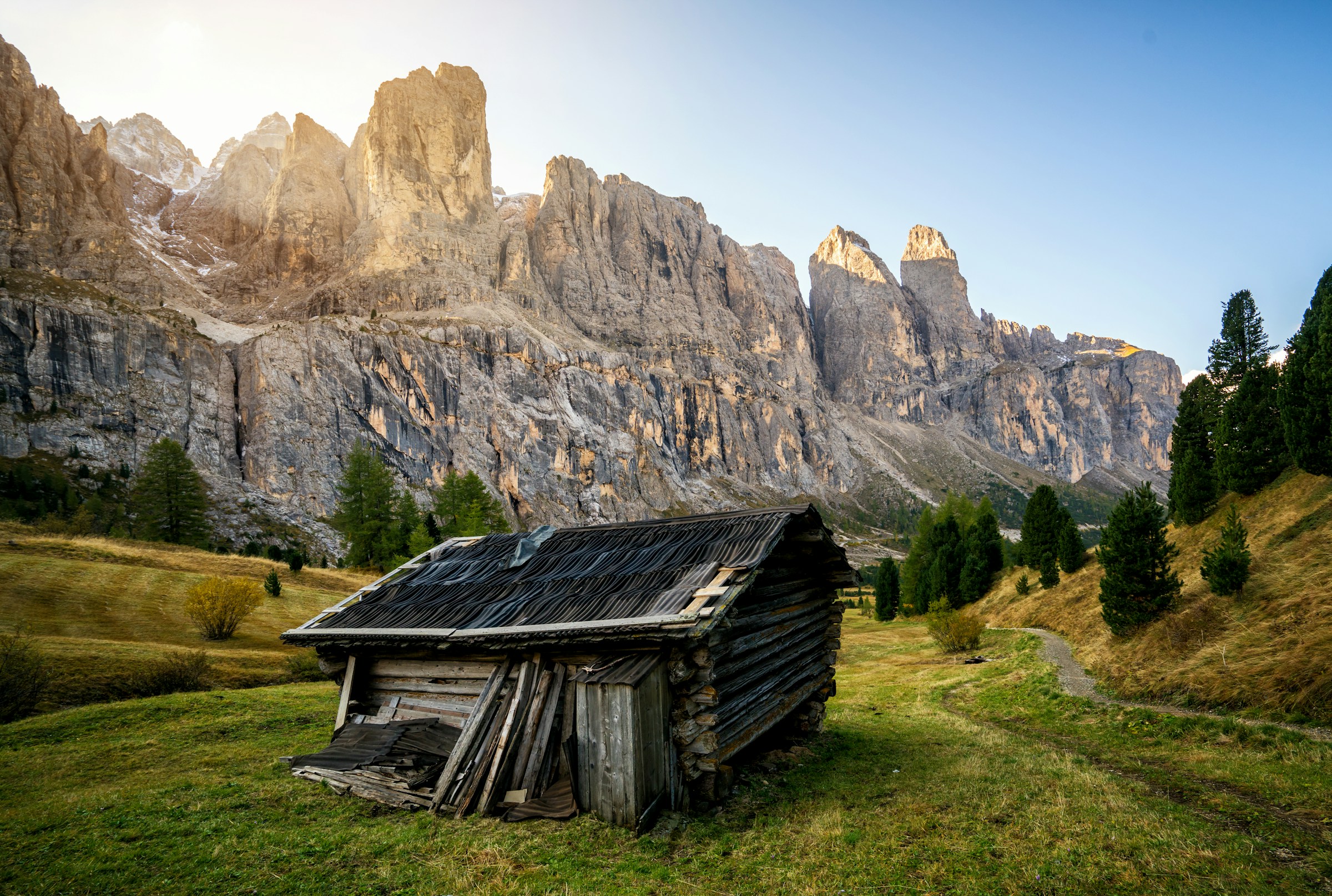 En ensom hytte står i en grøn dal mellem mægtige klipper i Val Gardena med en solopgang i baggrunden