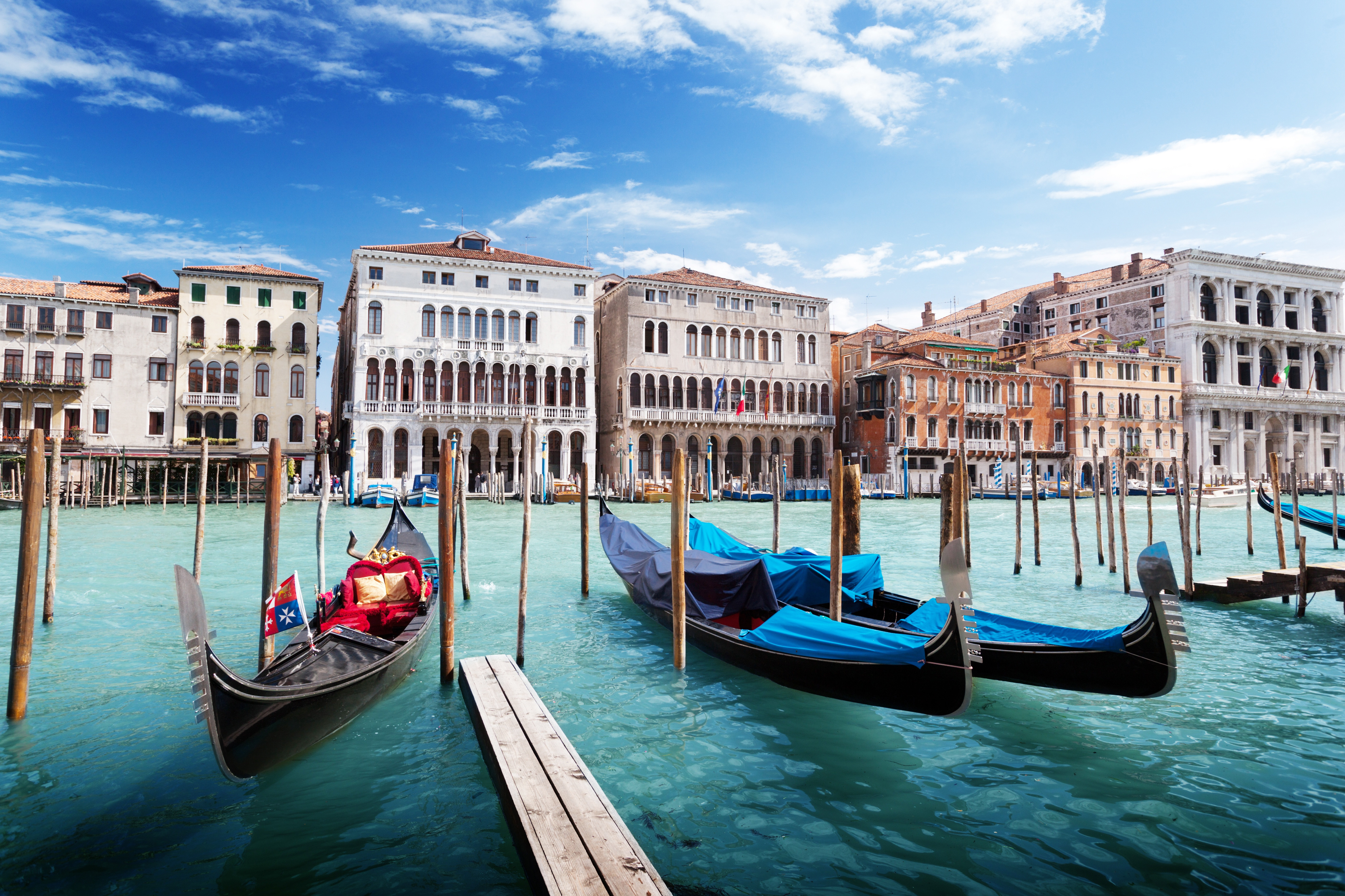 Gondoler ved Grand Canal i Venedig, Italien, med smukke historiske bygninger i baggrunden under en klar blå himmel