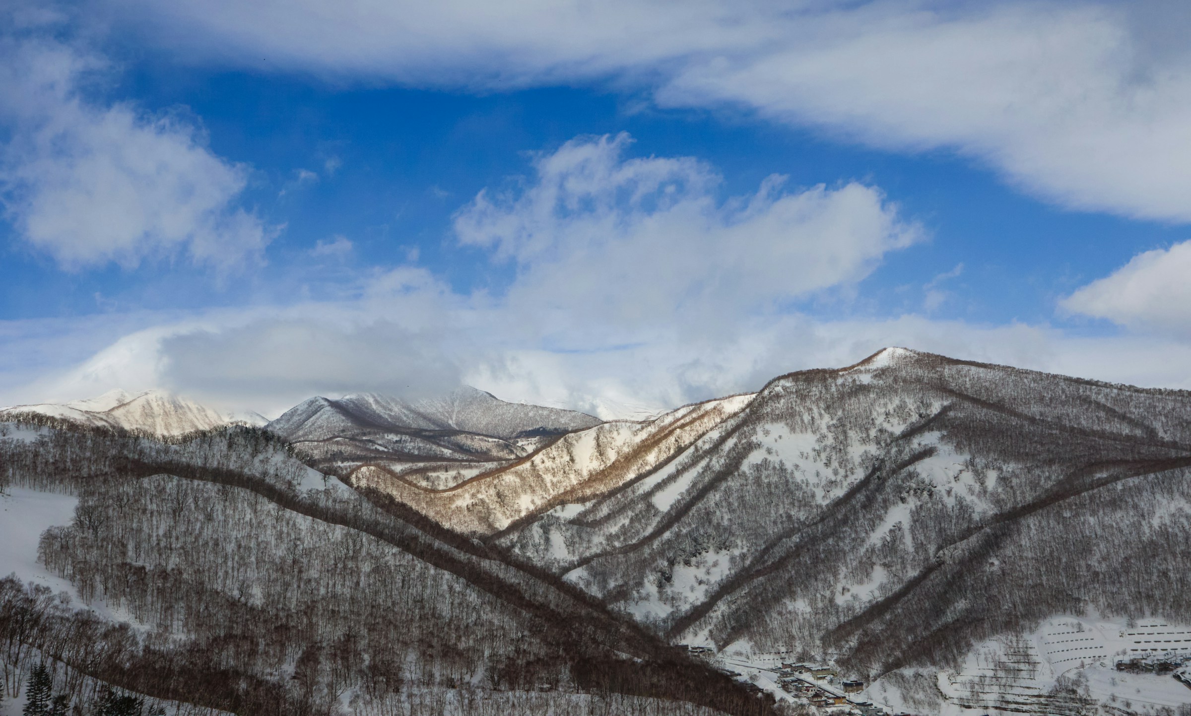 Sneklædte bjerge under en klar blå himmel med skyer i Hokkaido, Japan.