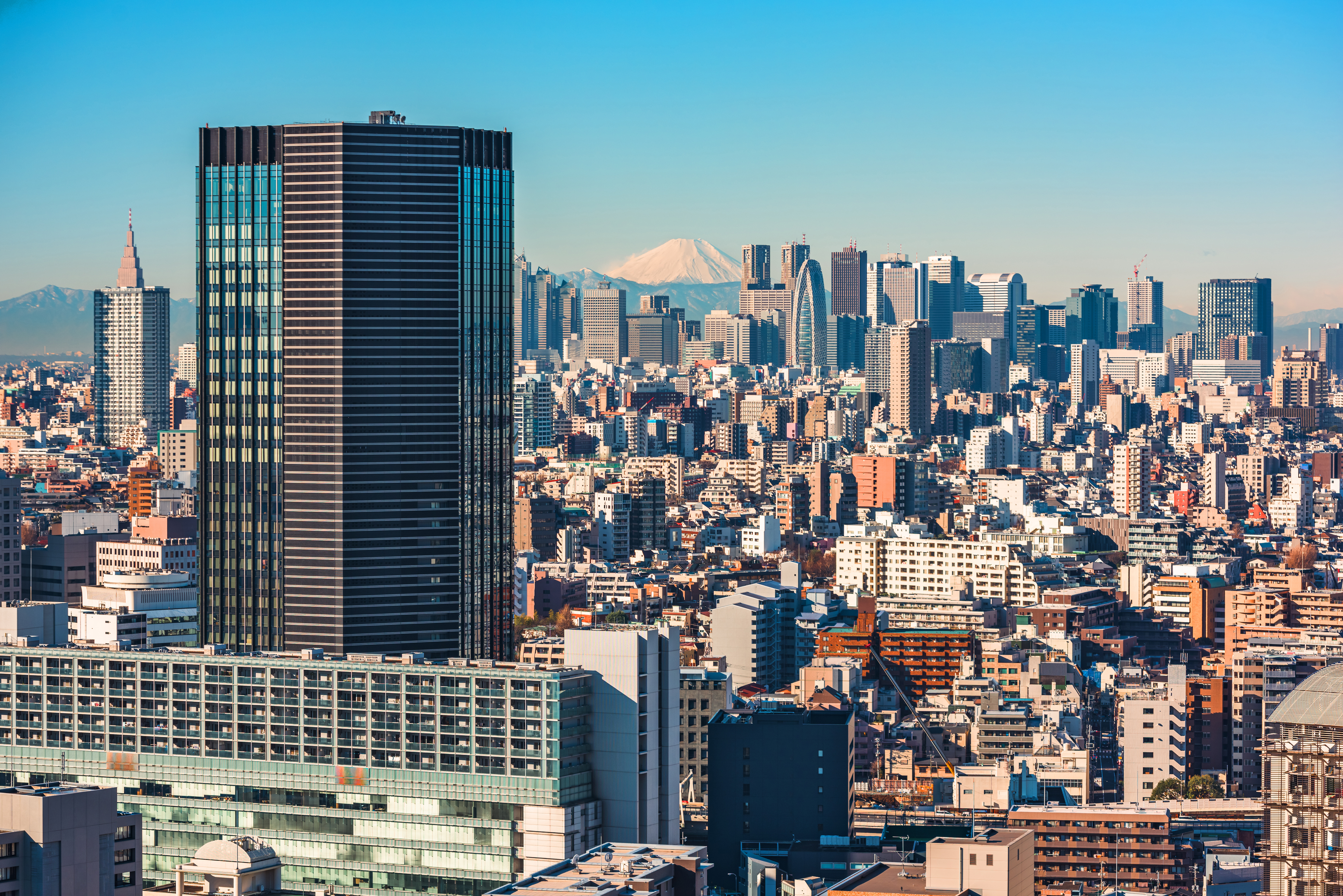 Skyline af Tokyo med moderne højhuse og ikonisk udsigt til Mount Fuji i baggrunden under en klar blå himmel