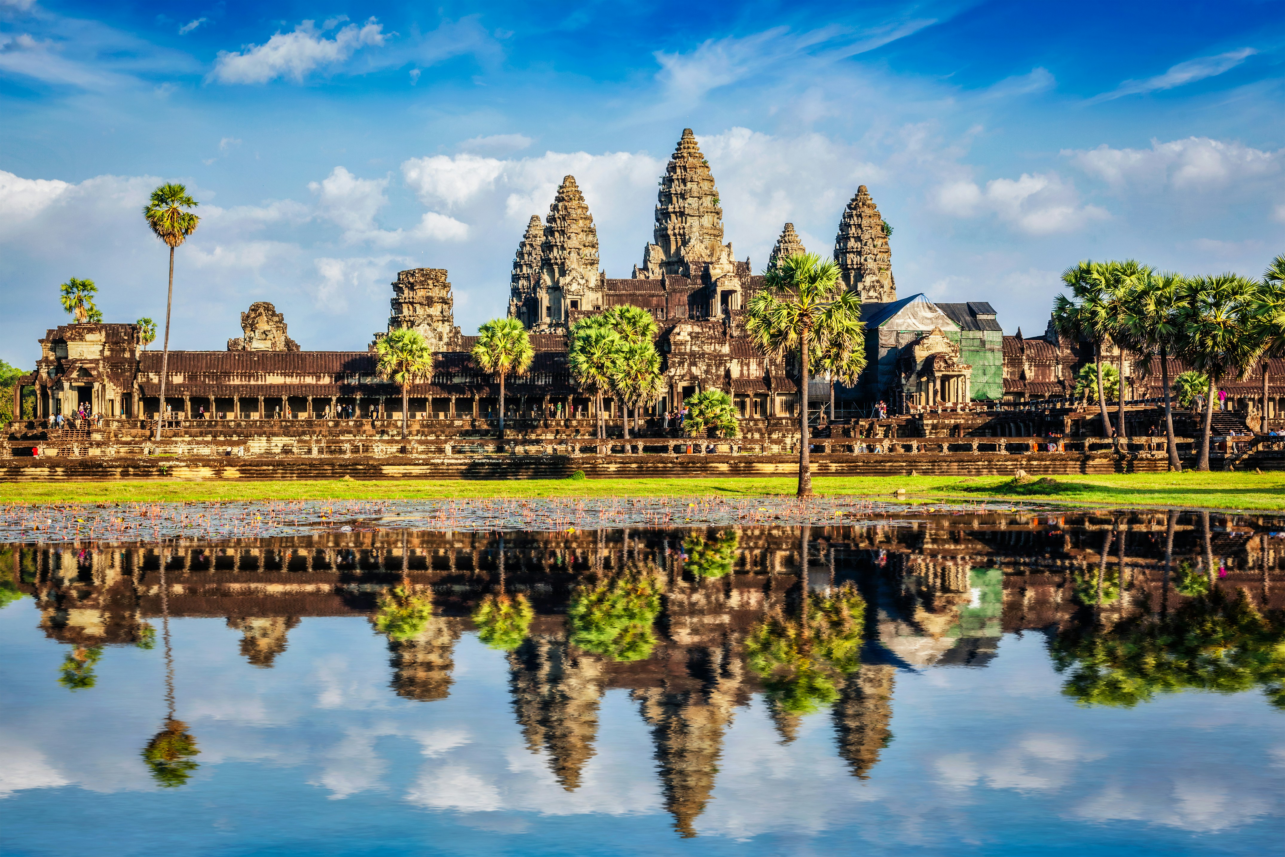 Angkor Wat-templet i Cambodja med reflektion i vandet, omgivet af palmer og blå himmel