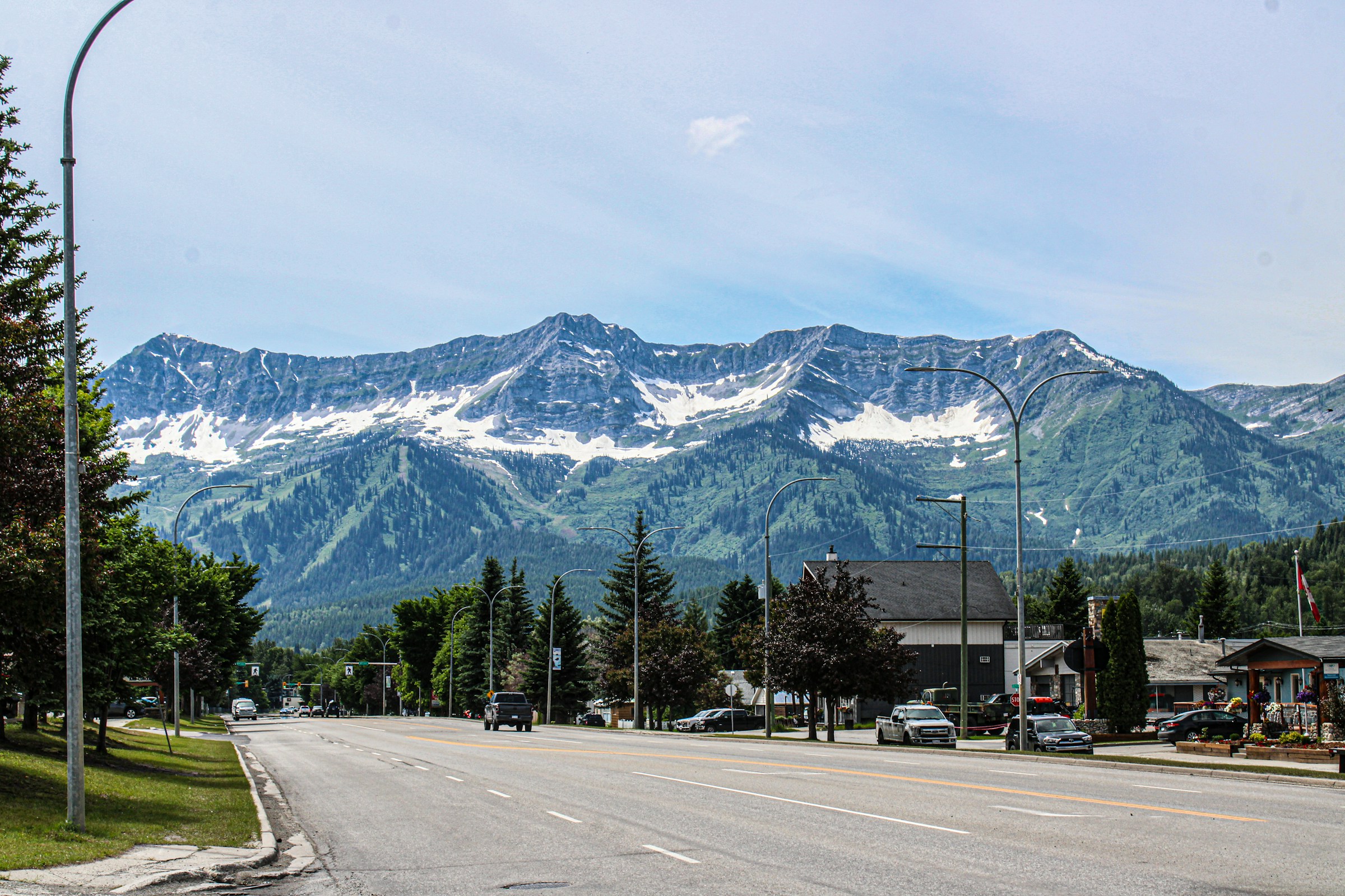 Bygade med udsigt over sneklædte bjergtoppe og grønne skråninger under en klar blå himmel i Fernie, Canada.