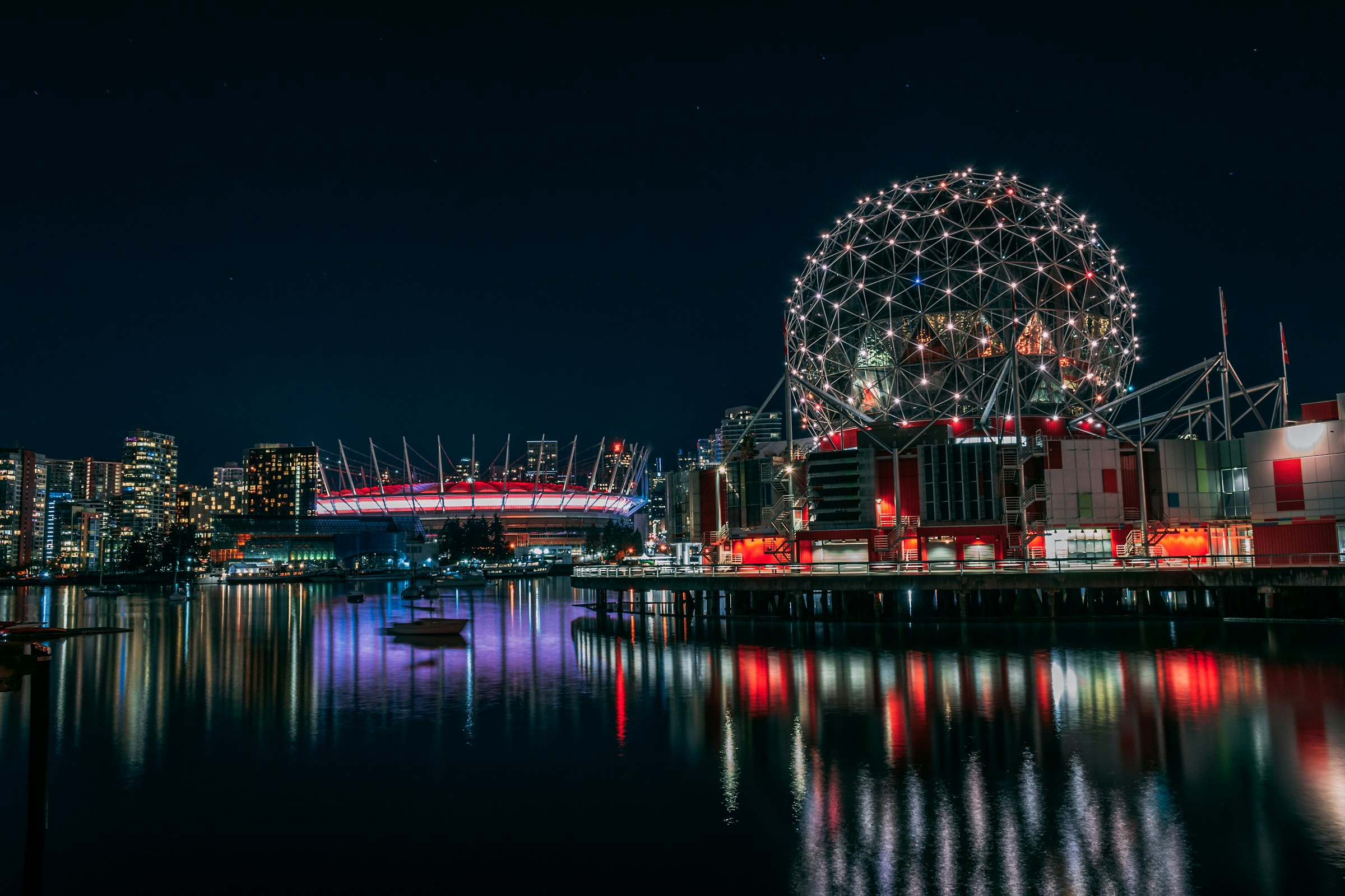 Night view of Vancouver's waterfront featuring the illuminated BC Place Stadium and Science World.