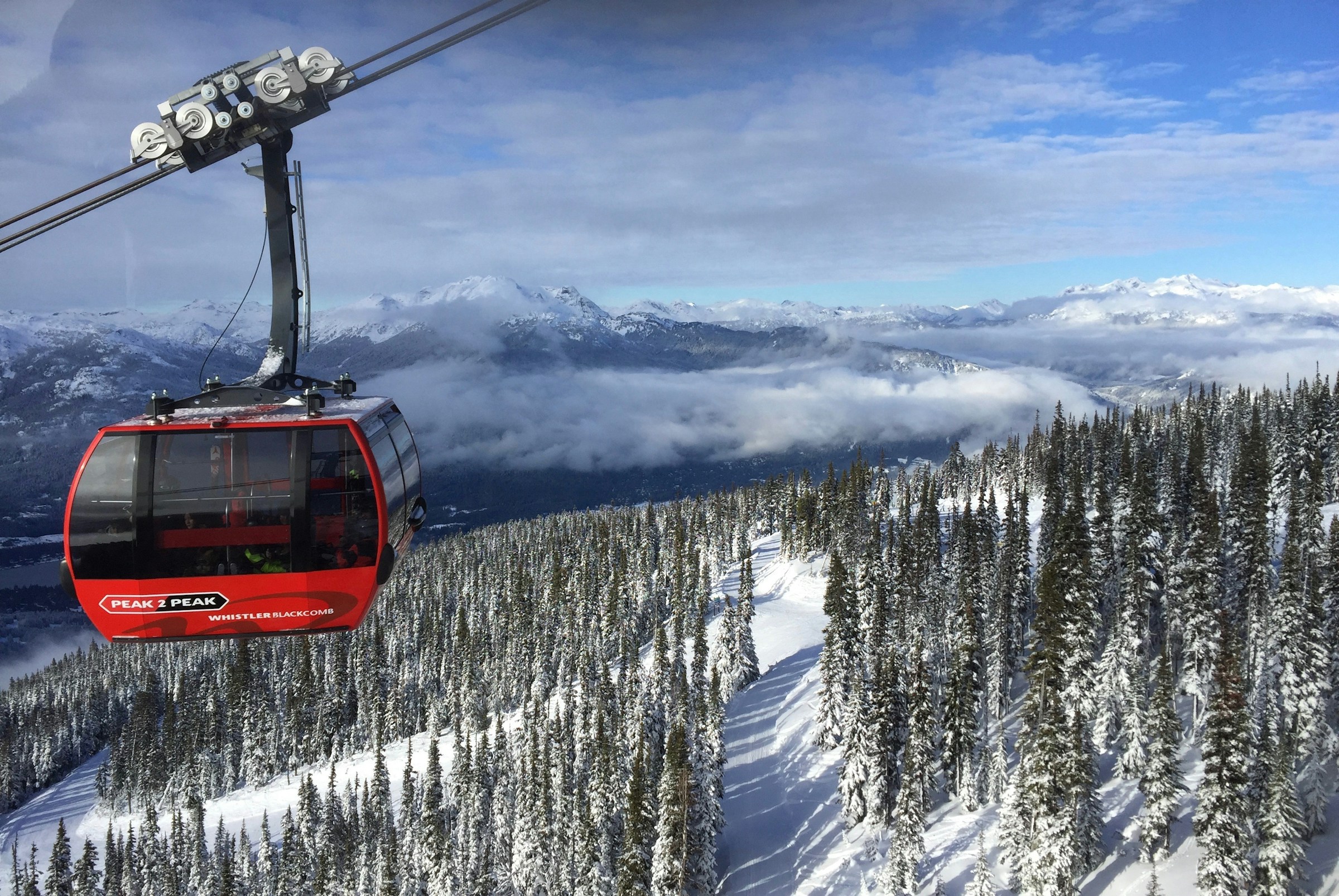 Rød gondollift med sneklædte bjerge og skove i baggrunden i Whistler Blackcomb, perfekt til skiløb og bjergturisme.