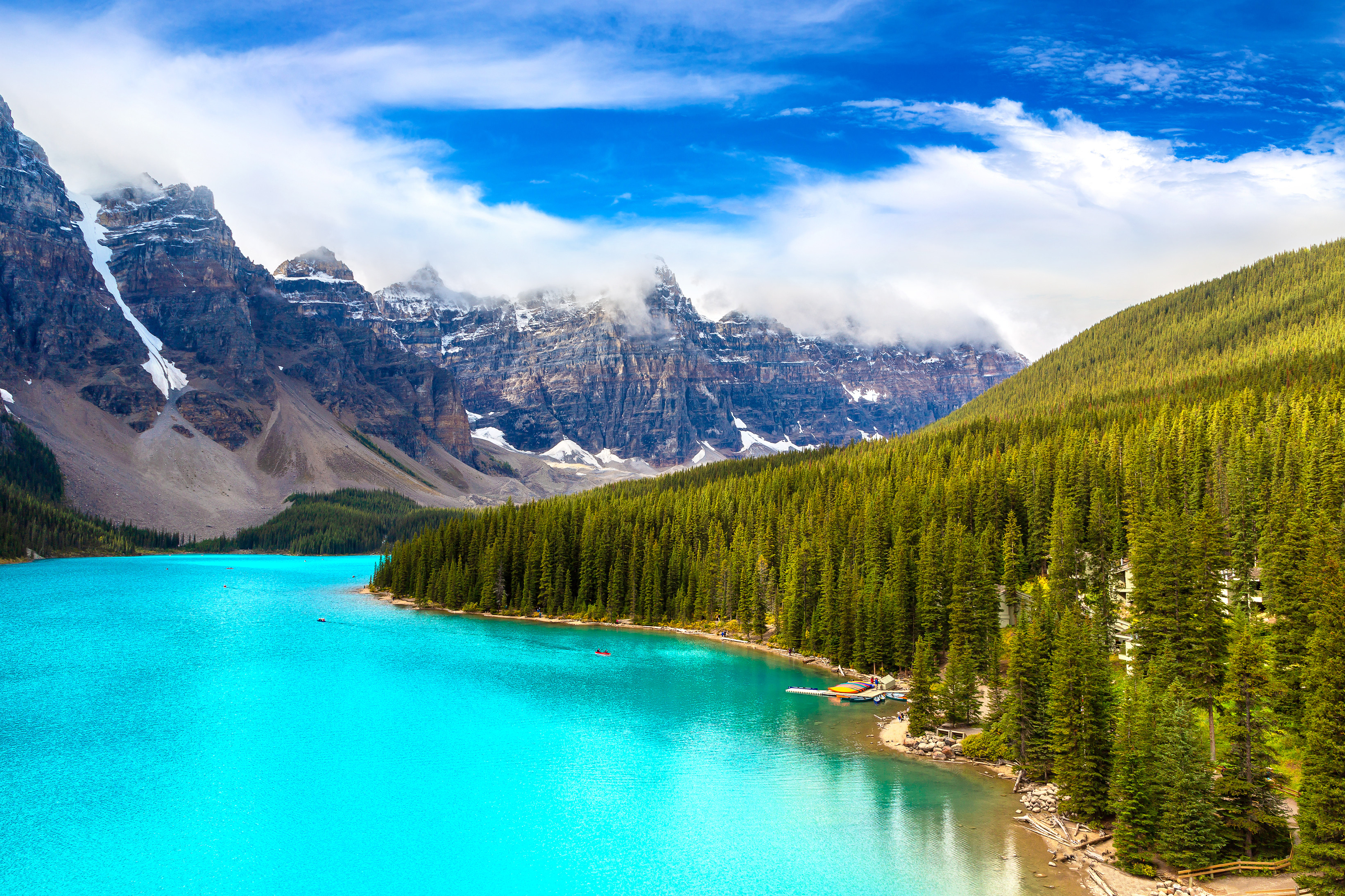 Azurblåt vand i Moraine Lake, Canada omgivet af majestætiske bjerge og frodige granskove under en klar himmel