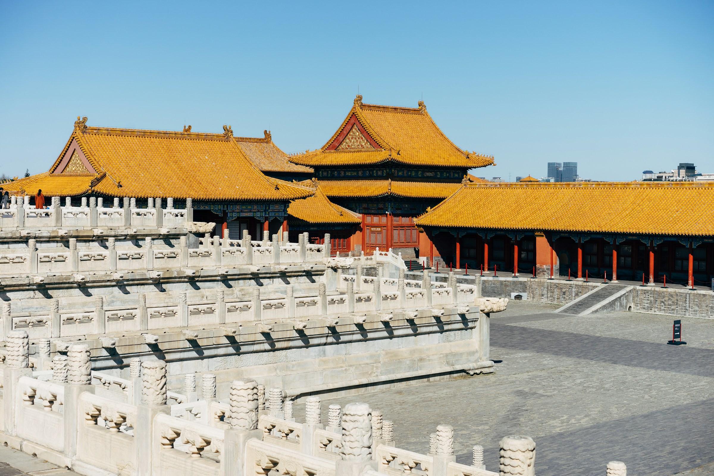 Ancient Chinese architecture with traditional yellow-tiled roofs and detailed stone carvings under a clear blue sky, possibly part of the Forbidden City in Beijing